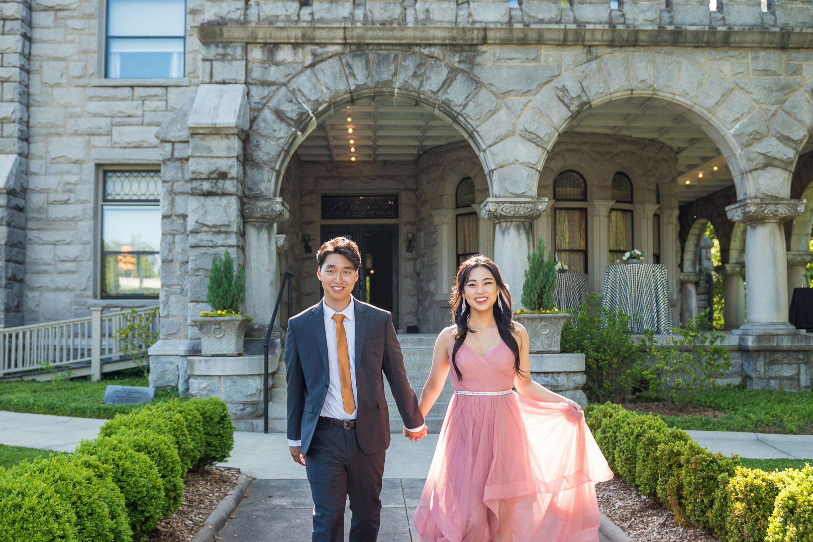Couple walking hand in hand along the garden path in front of Rhodes Hall