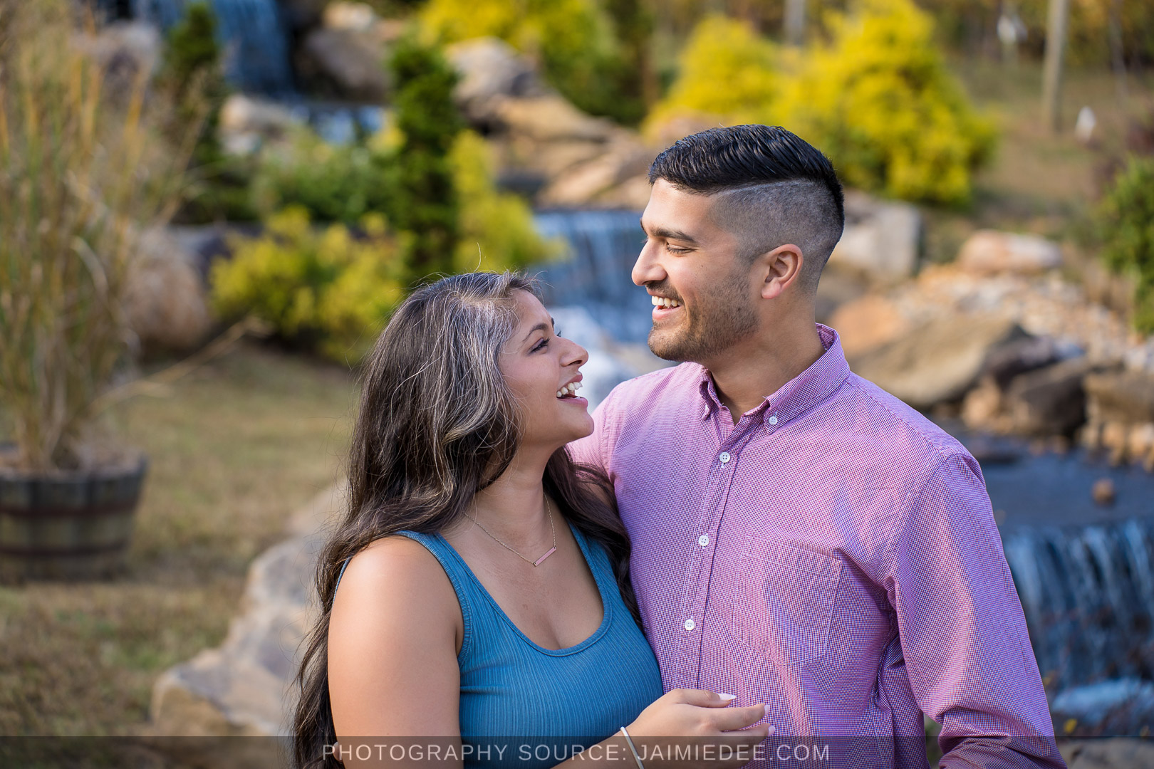 Engaged couple smiling at each other in front of the waterfall at Big Door Vineyards