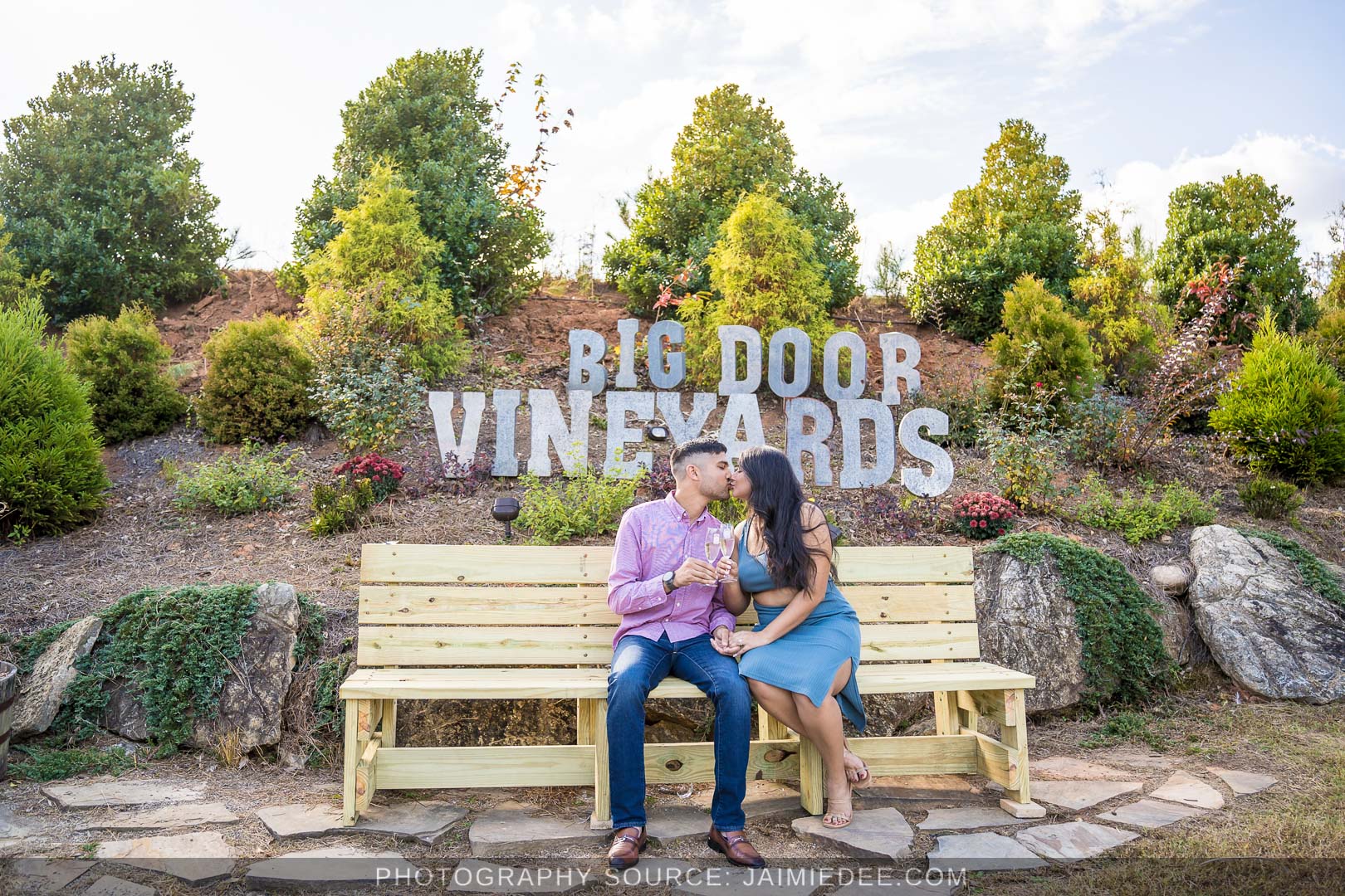 Engaged couple kissing on the bench beneath the Big Door Vineyards sign