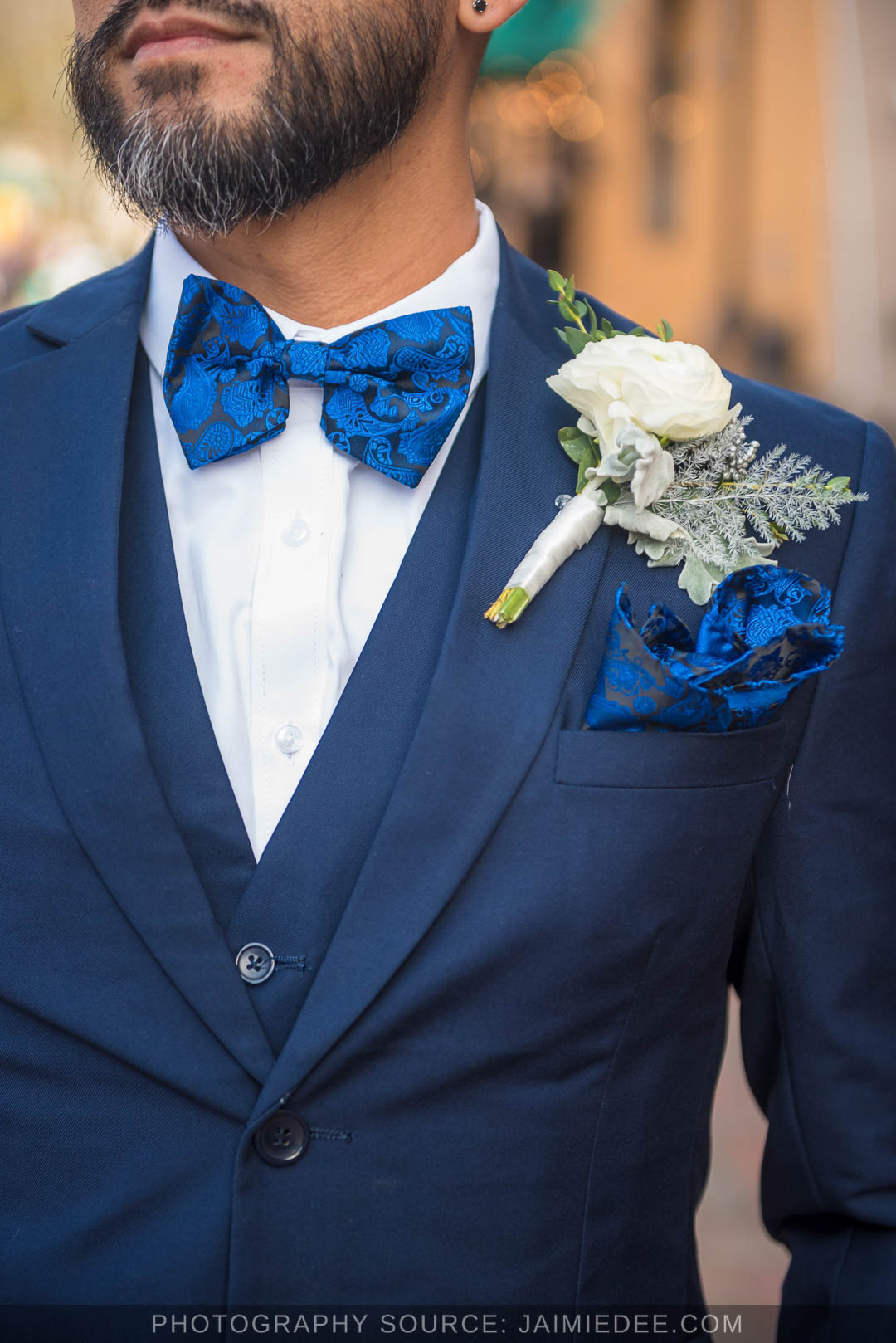 Close up of a navy suit with a blue bow tie and white rose boutonniere