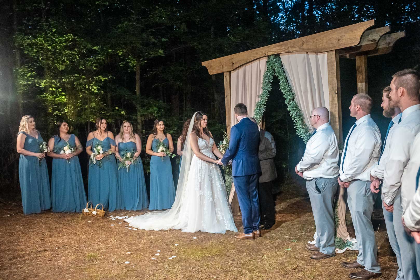 Bride and groom at an outdoor evening ceremony with bridesmaids in dusty blue gowns