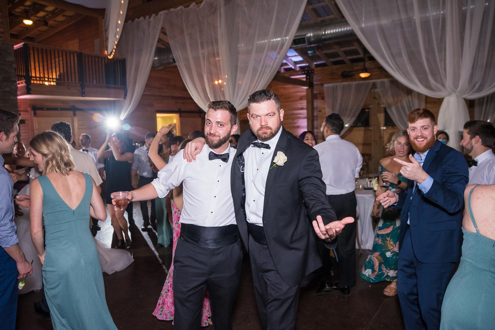 Groom and groomsmen dancing with guests at a lively wedding reception