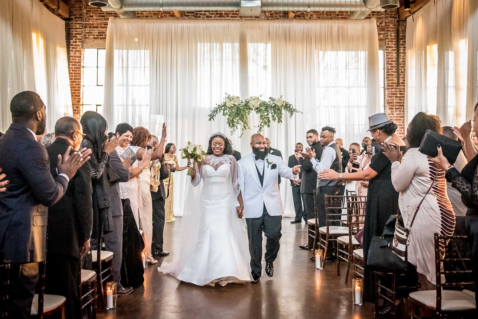 Newlyweds walking back up the aisle as guests applaud after an indoor wedding ceremony