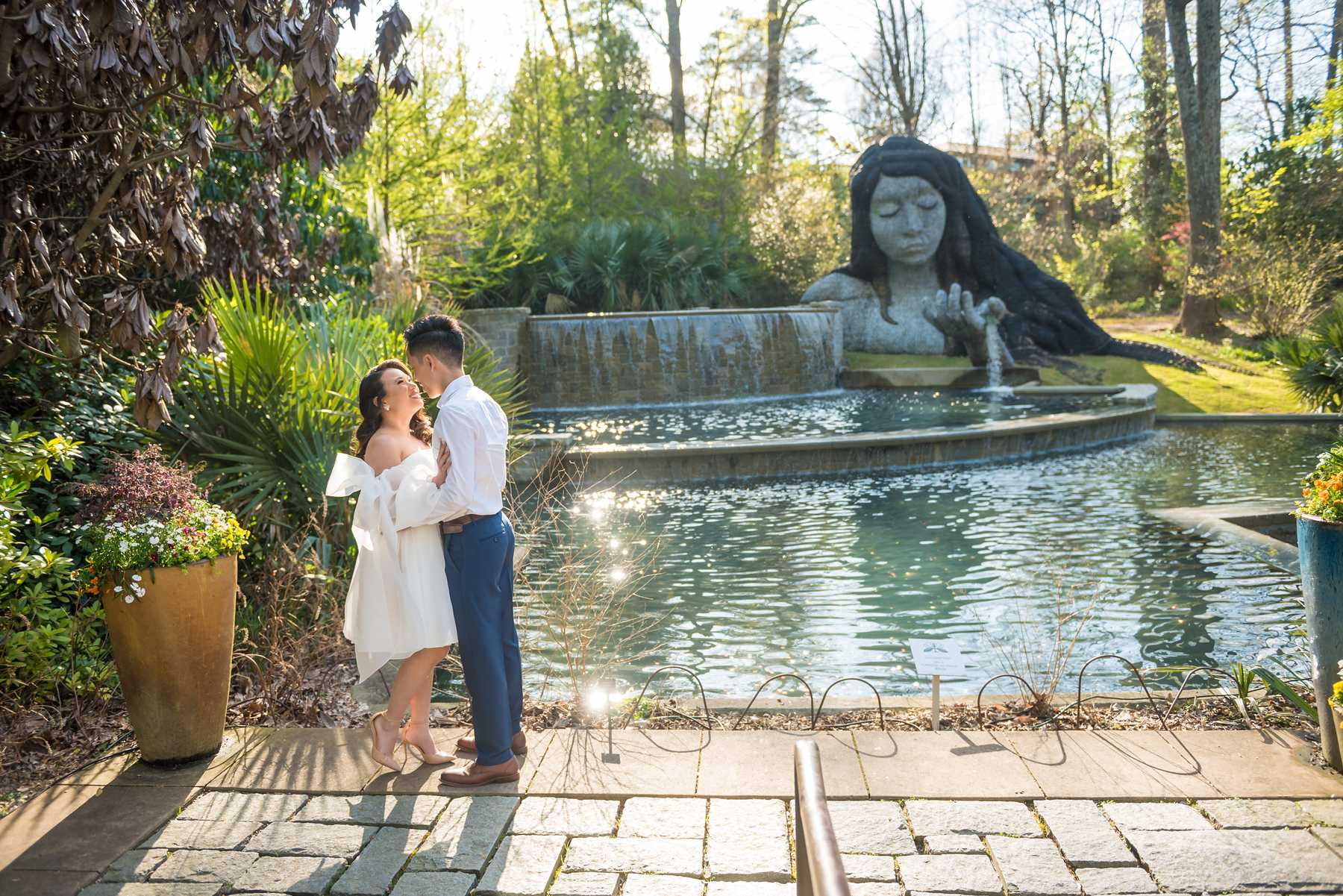 Couple in a white dress and blue pants by the Earth Goddess pool in spring at the Atlanta Botanical Garden