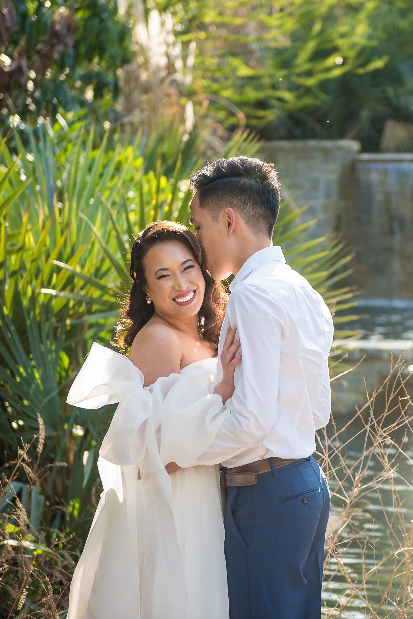 Smiling couple close together by the waterfall pool in golden spring light