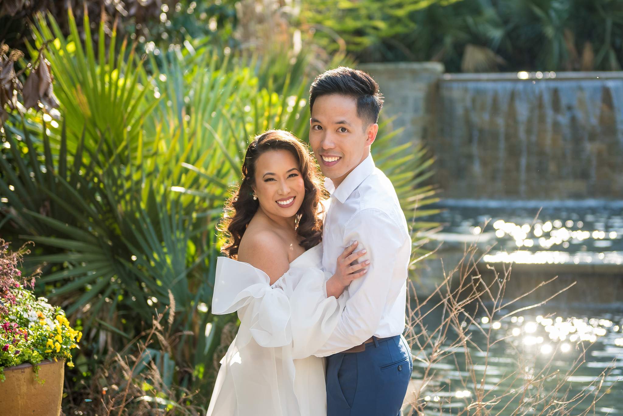 Bride-to-be in an off-the-shoulder white dress laughing with her partner by the garden pool