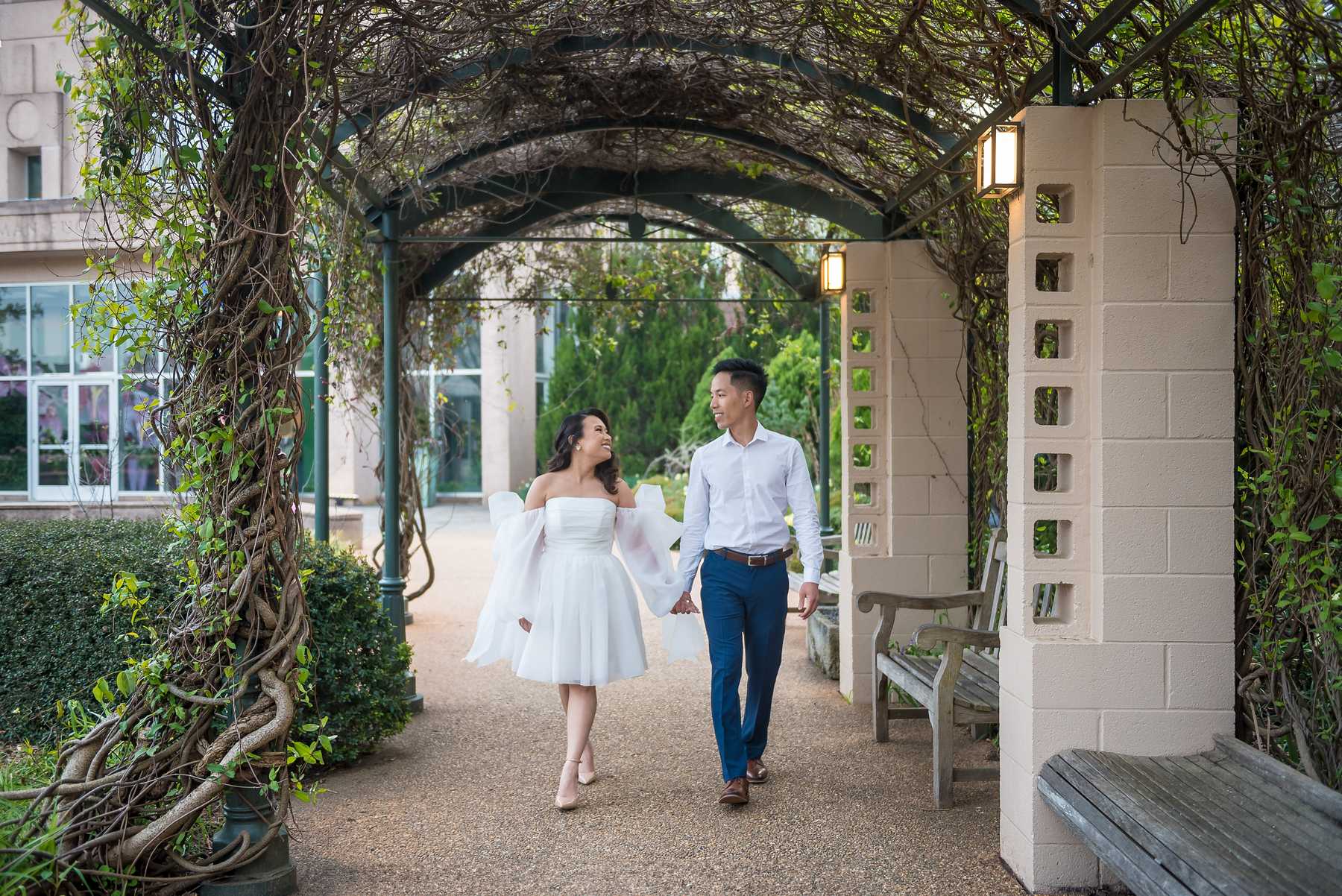 Couple walking hand in hand beneath the vine-covered arbor at the Atlanta Botanical Garden