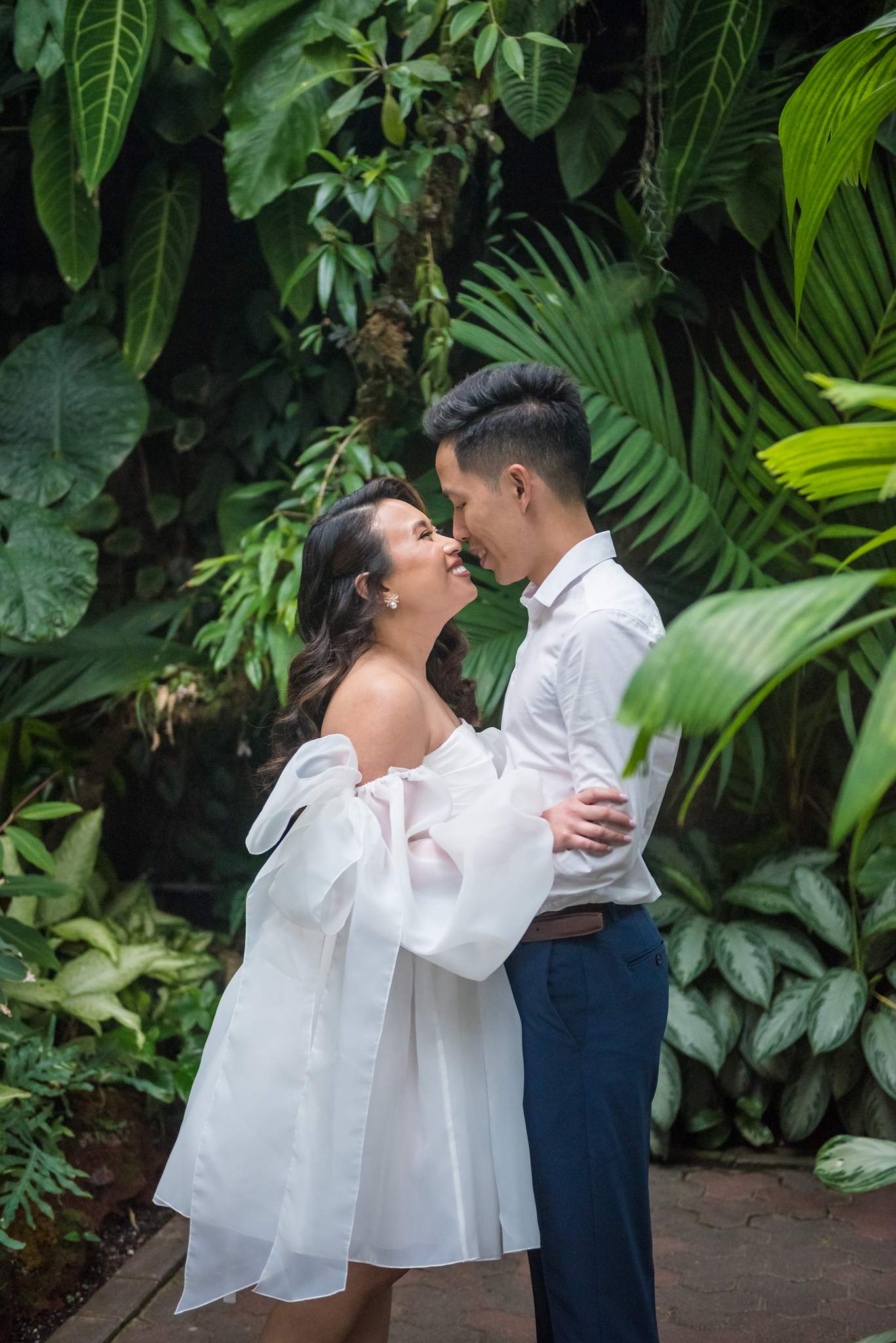 Vertical photo of a couple about to kiss among tropical leaves in the conservatory