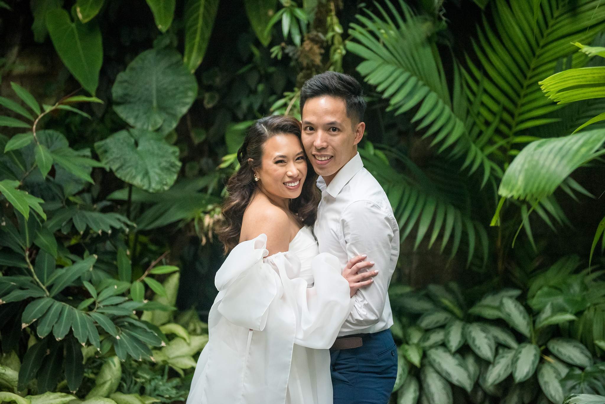 Smiling couple surrounded by large green tropical leaves in the Fuqua Conservatory