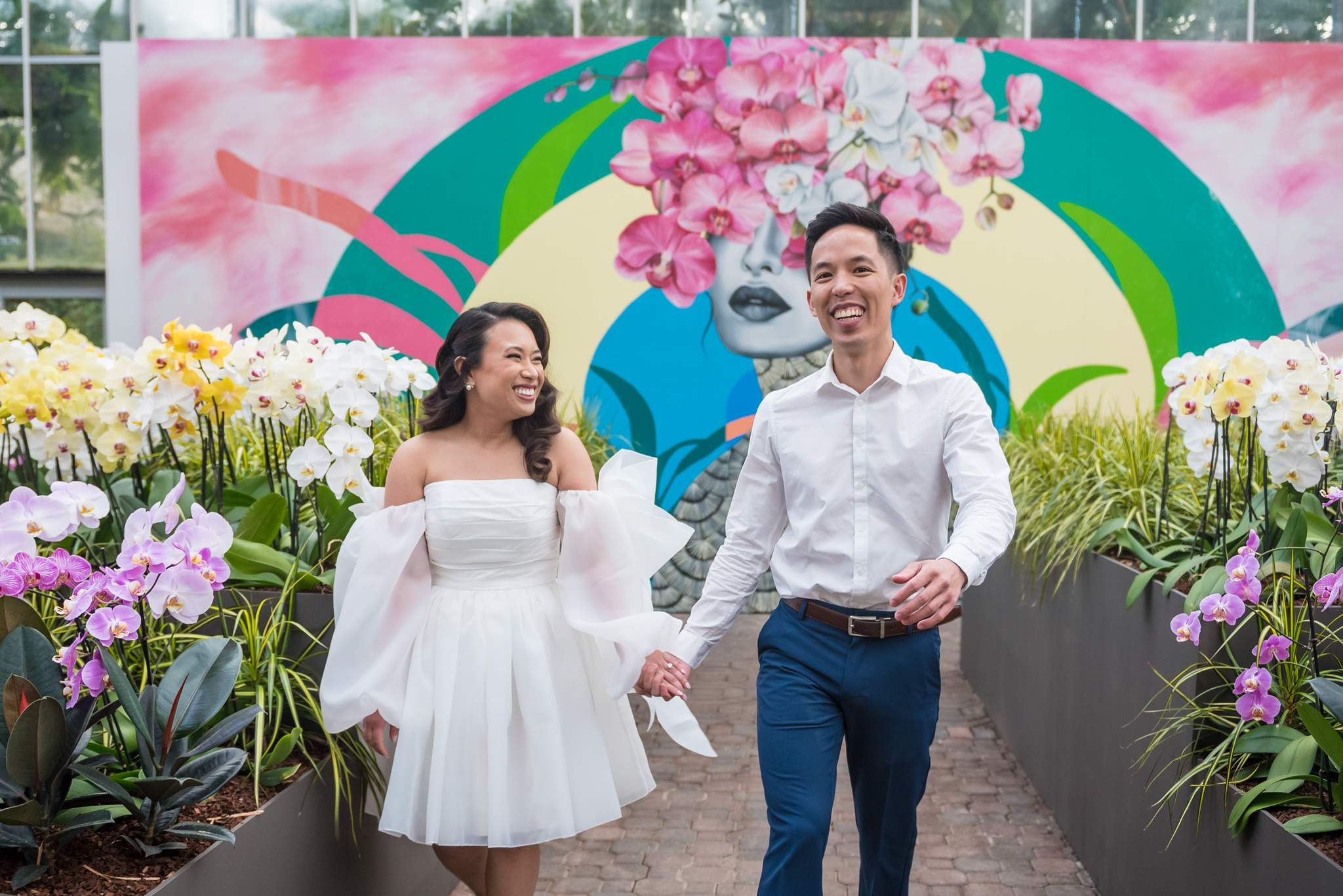 Couple walking hand in hand between orchid beds in front of a colorful mural