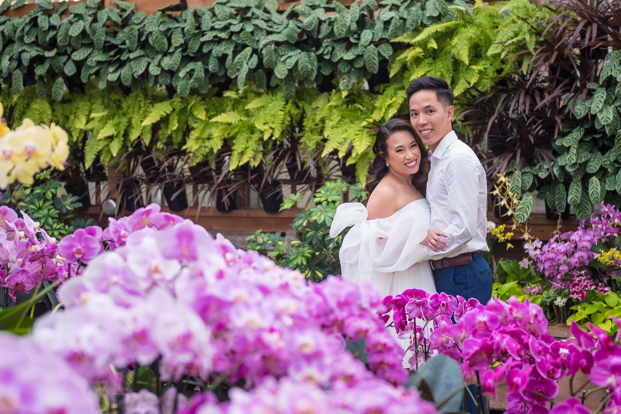 Bride-to-be smiling up at her partner surrounded by purple and pink orchids