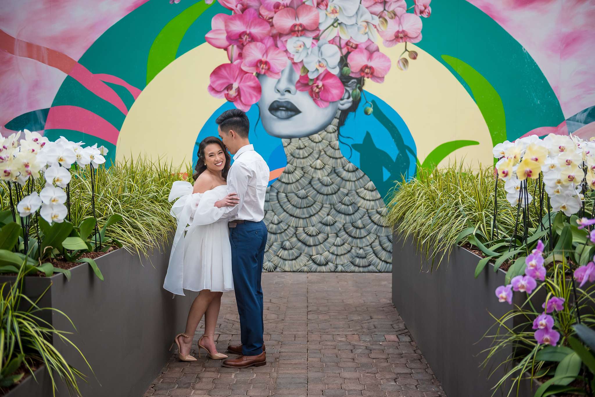 Couple standing in front of a vivid orchid mural with white orchids