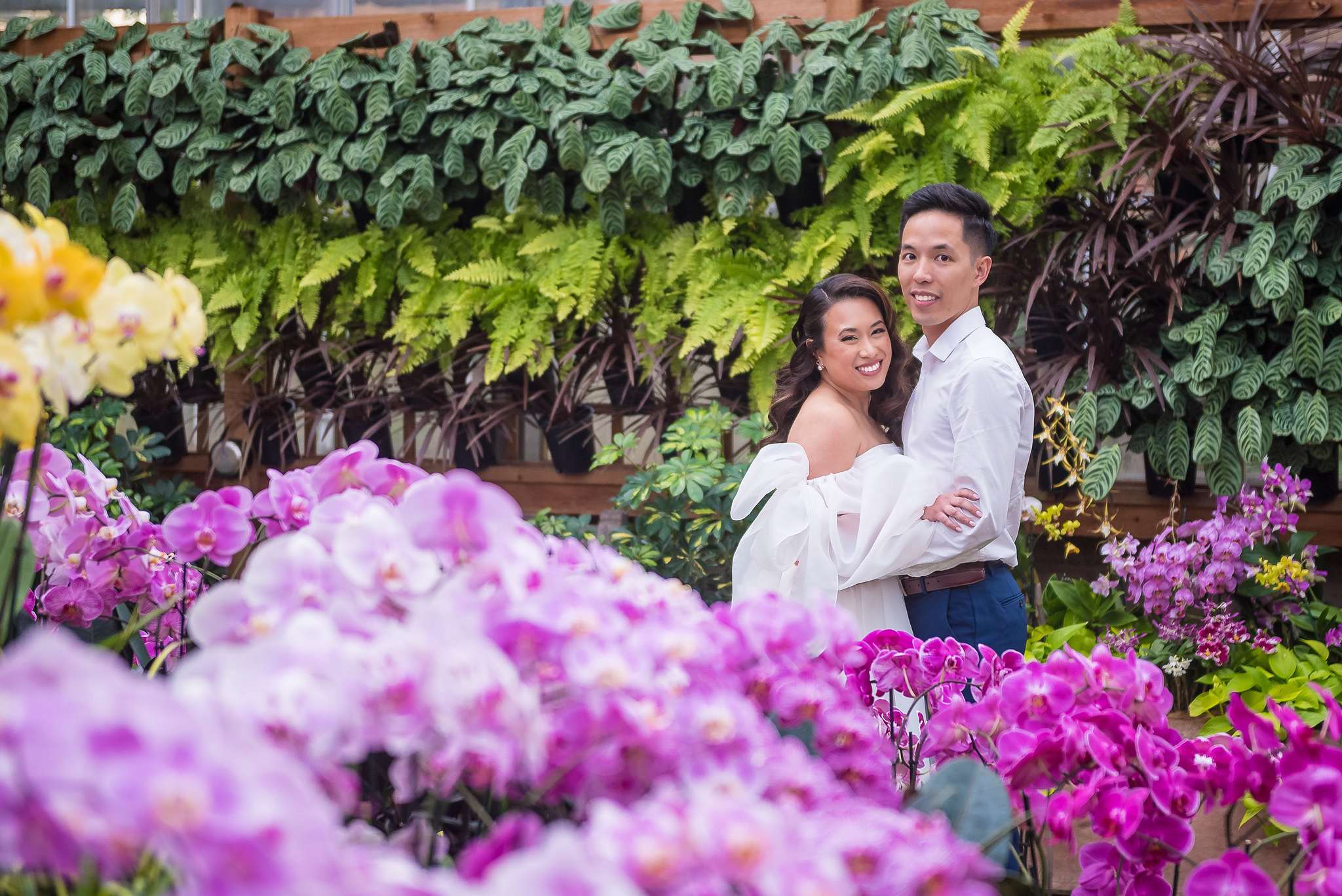 Close portrait of a smiling bride-to-be with her partner behind pink and purple orchids