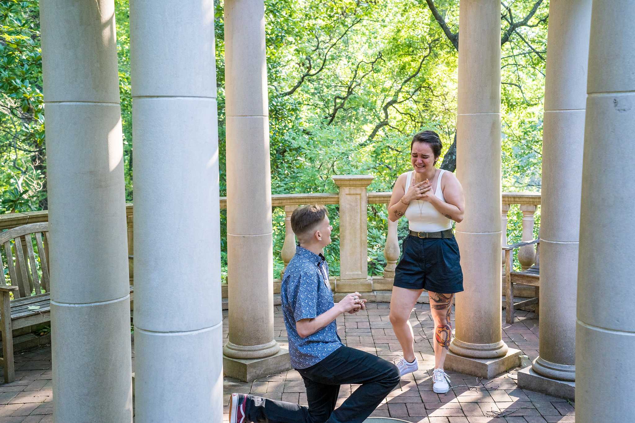 Partner kneels with a ring as the other covers their mouth in surprise inside the garden gazebo