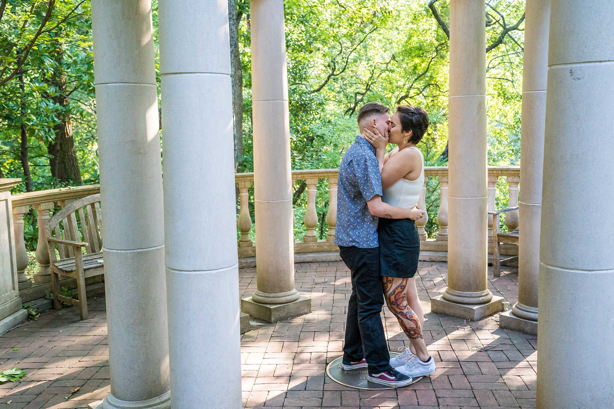 Newly engaged couple kissing between the stone columns of the garden gazebo