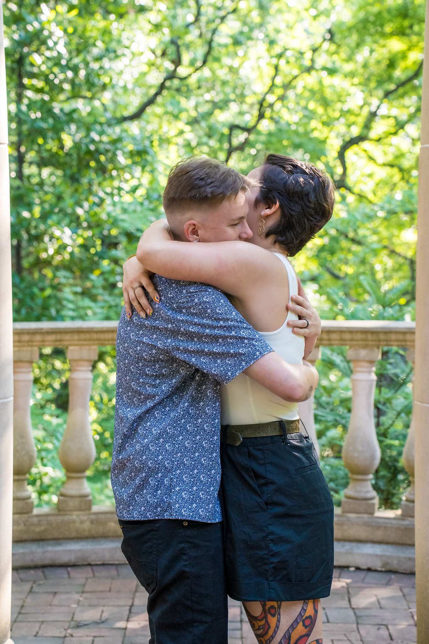 Joyful embrace after a proposal with green trees behind the gazebo railing