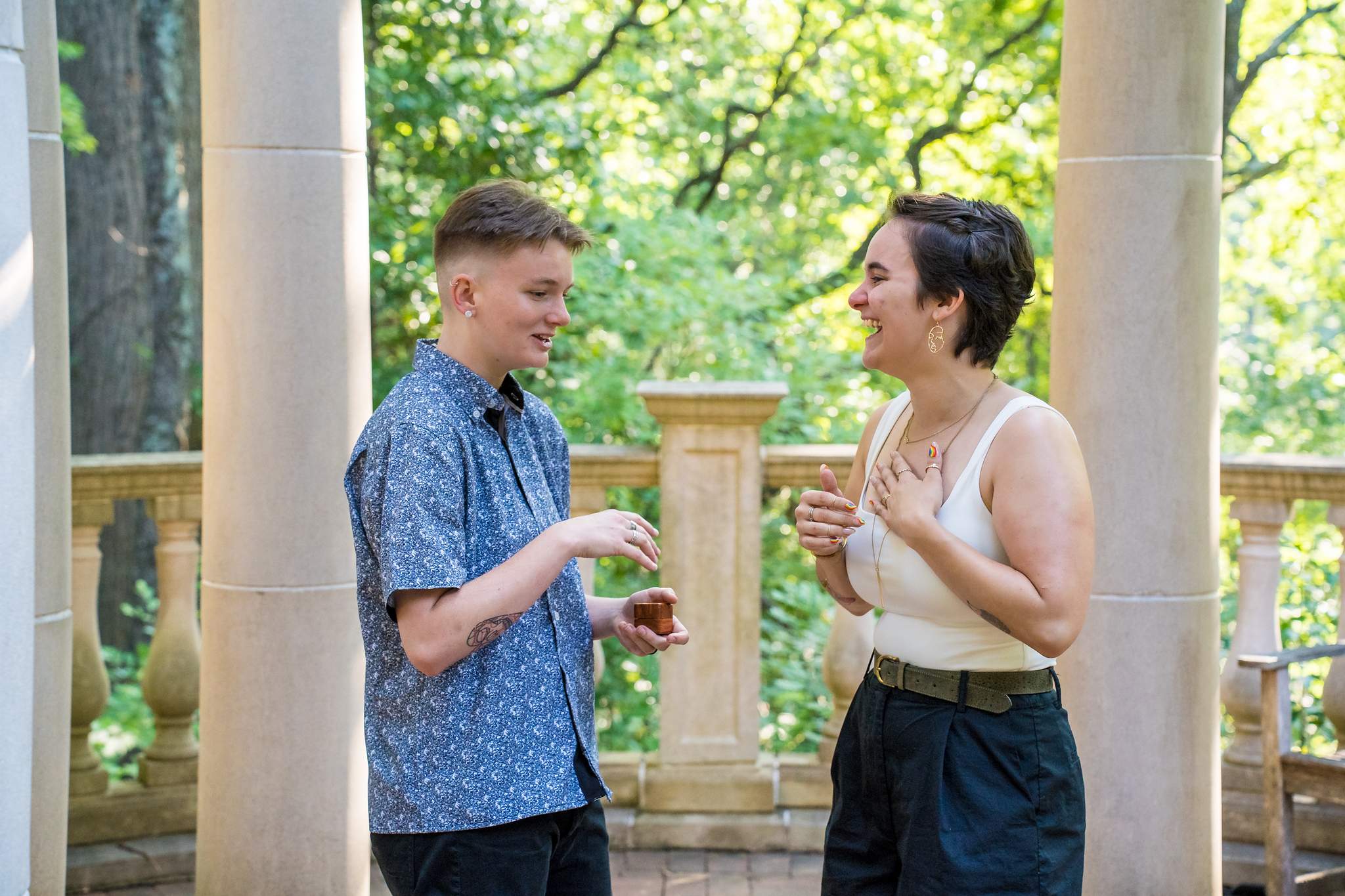 Newly engaged couple laughing as they look at the ring between the gazebo columns