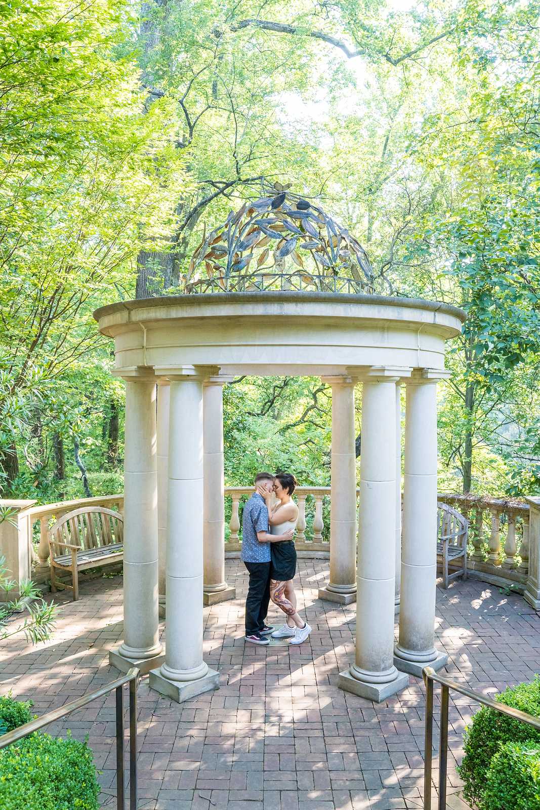 Newly engaged couple standing together inside the domed gazebo, seen from the garden path