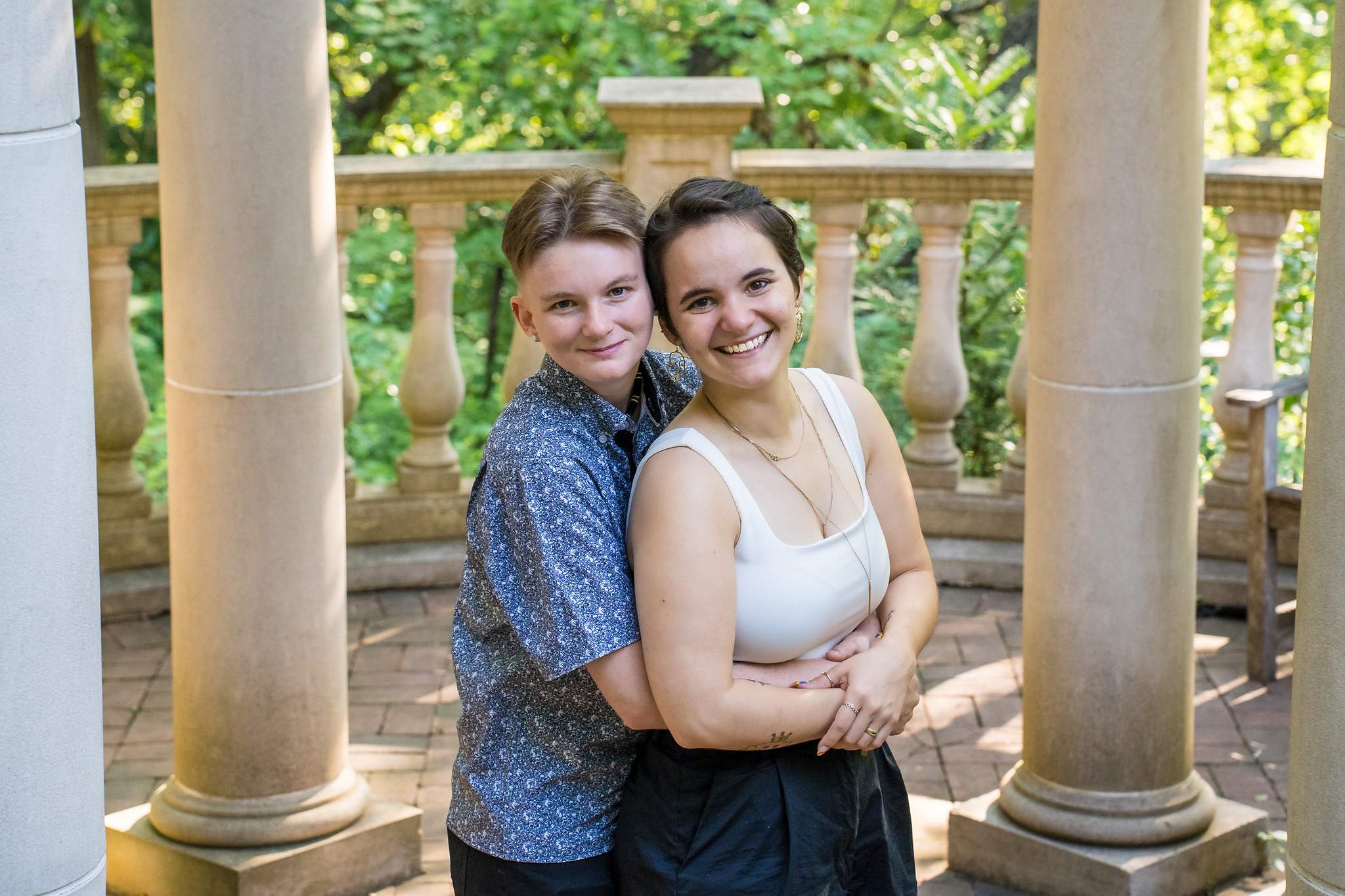 Smiling engaged couple cheek to cheek between the stone columns of the gazebo