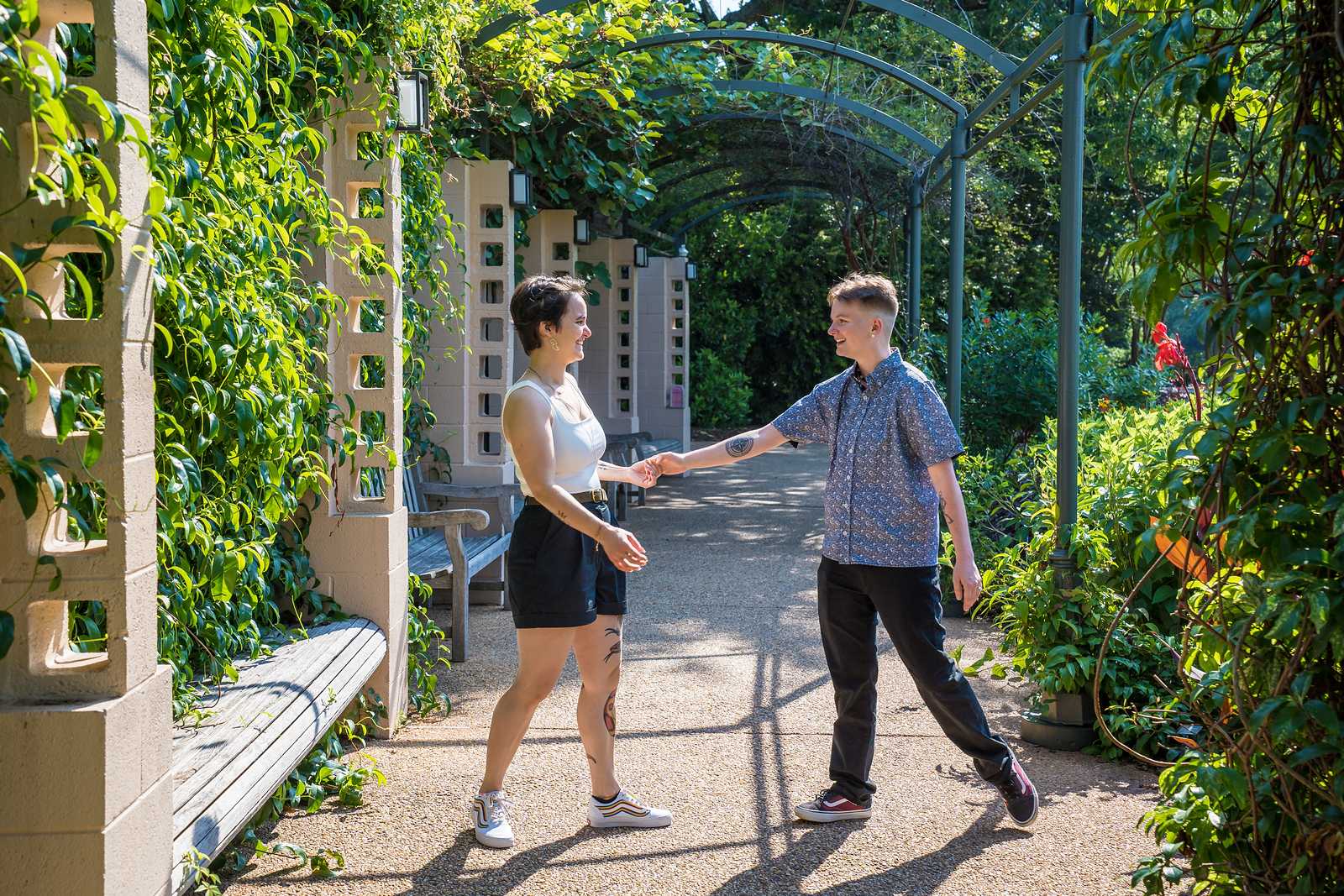 Engaged couple reaching for each other under the vine-covered arbor at the Atlanta Botanical Garden
