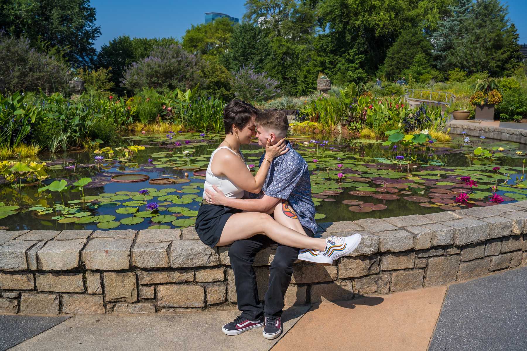 Engaged couple sitting on a stone wall beside the lily pond at the Atlanta Botanical Garden