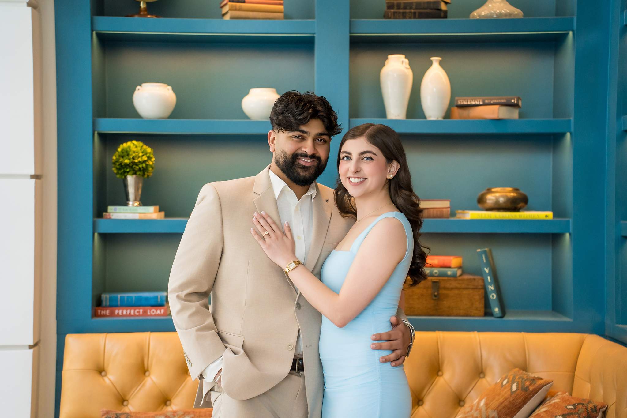 Engaged couple on a leather sofa in front of teal bookshelves at Chateau Elan
