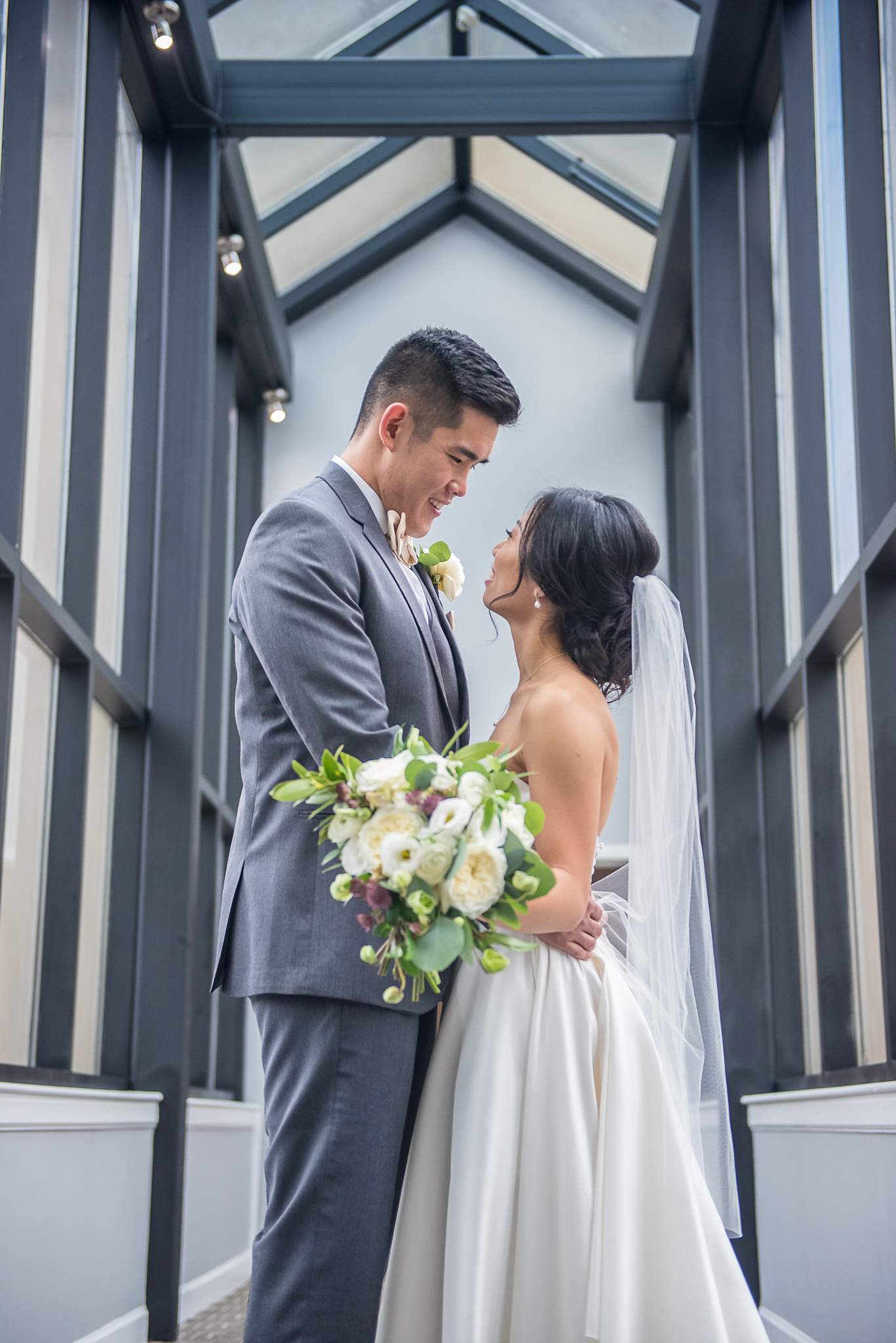 Bride and groom gaze at each other inside a skylit glass corridor at Chateau Elan
