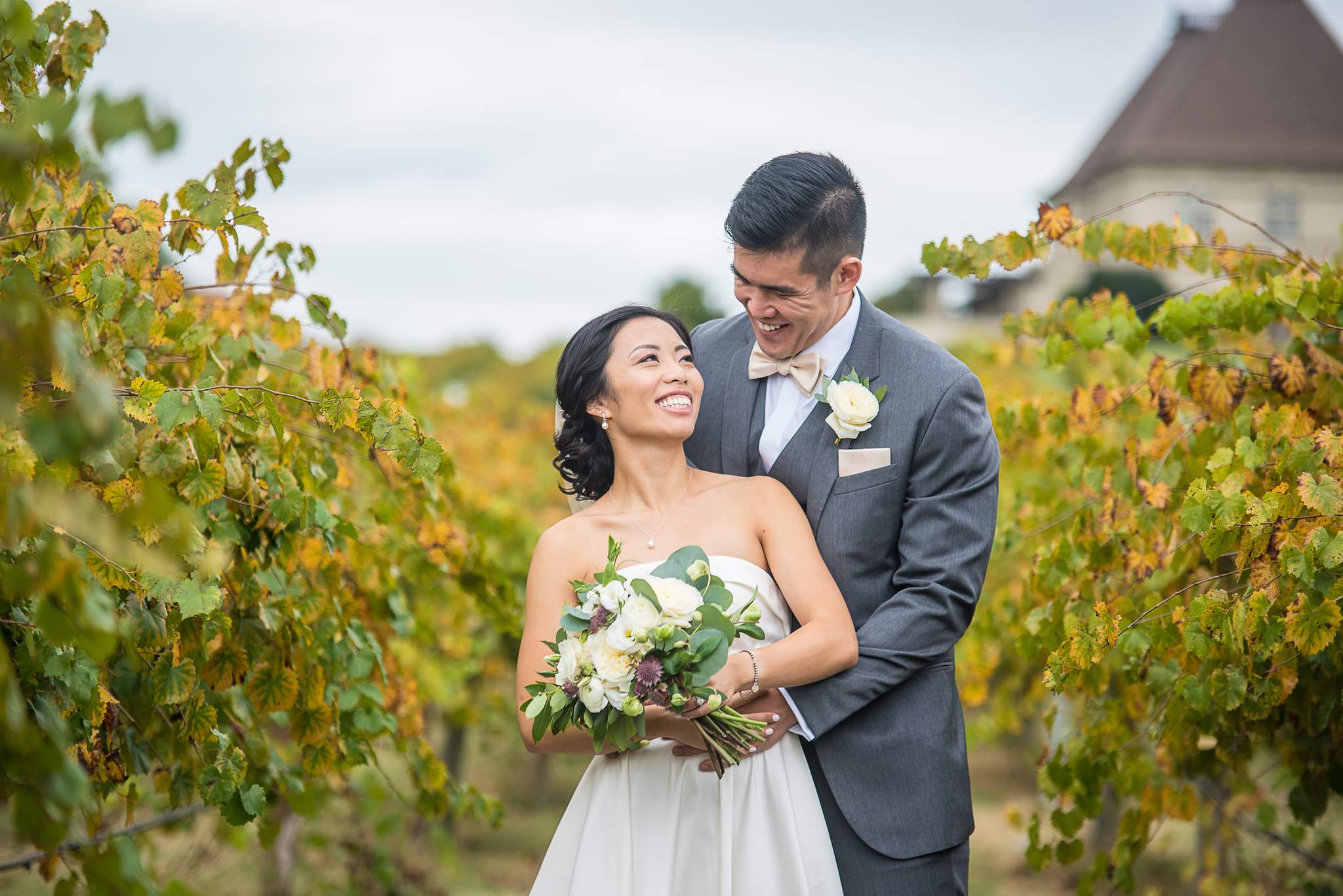 Bride laughs in the groom's arms among golden autumn grapevines with a chateau turret behind them