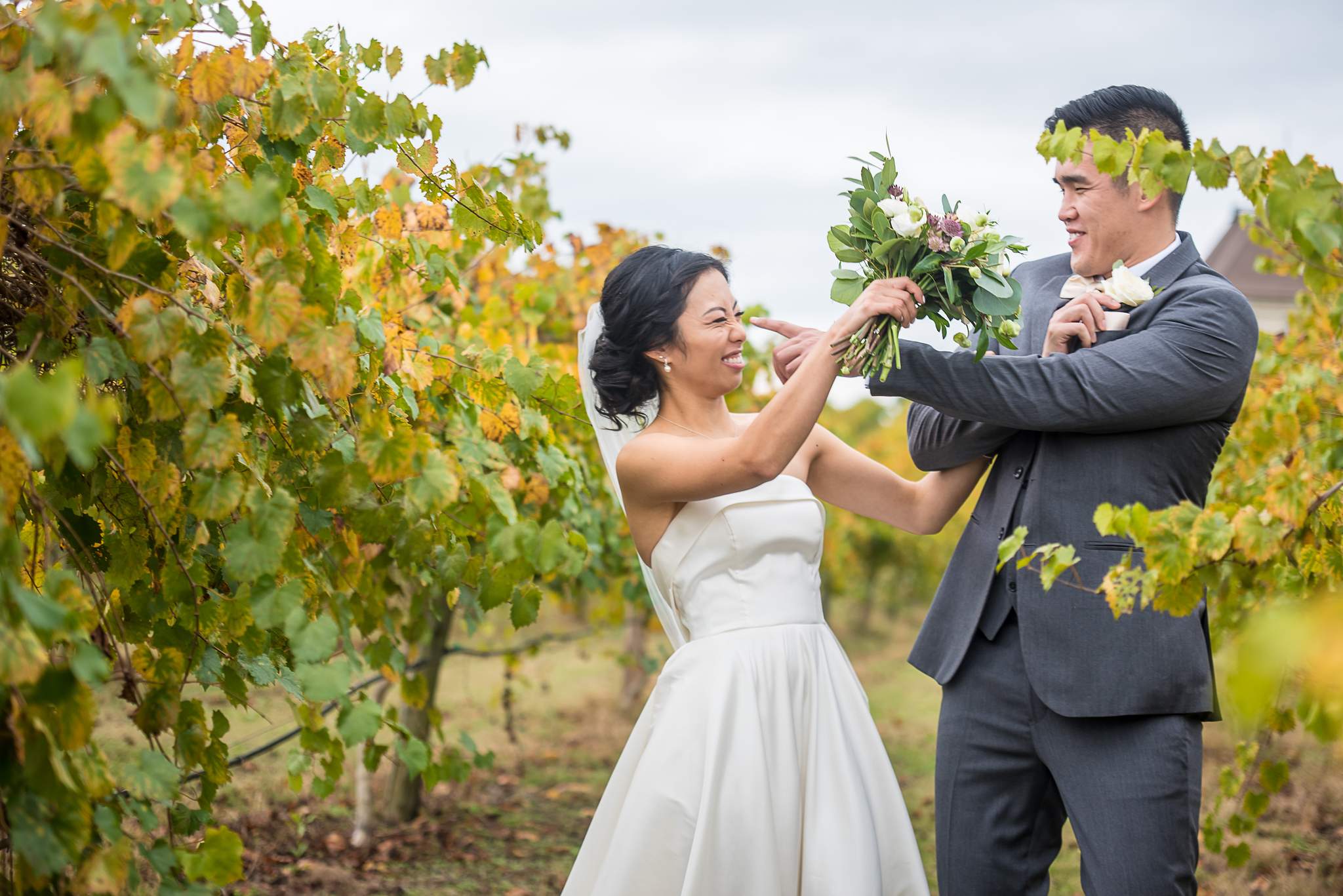 Bride and groom laugh and play with the bouquet among the autumn grapevines at Chateau Elan