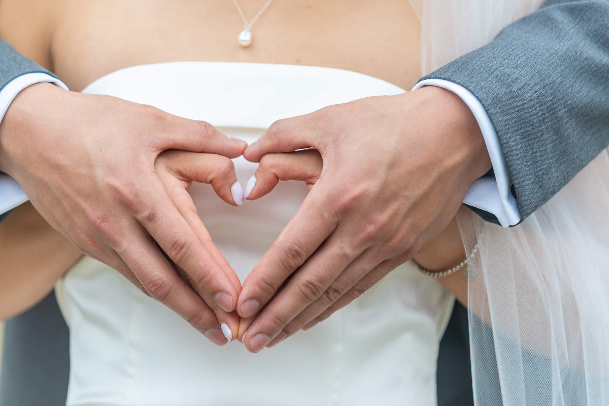 Bride and groom form a heart with their hands against her strapless satin wedding dress