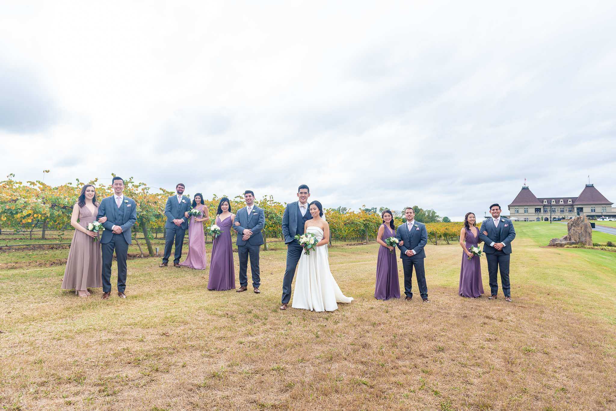 Full wedding party poses in the Chateau Elan vineyard field with the chateau in the distance