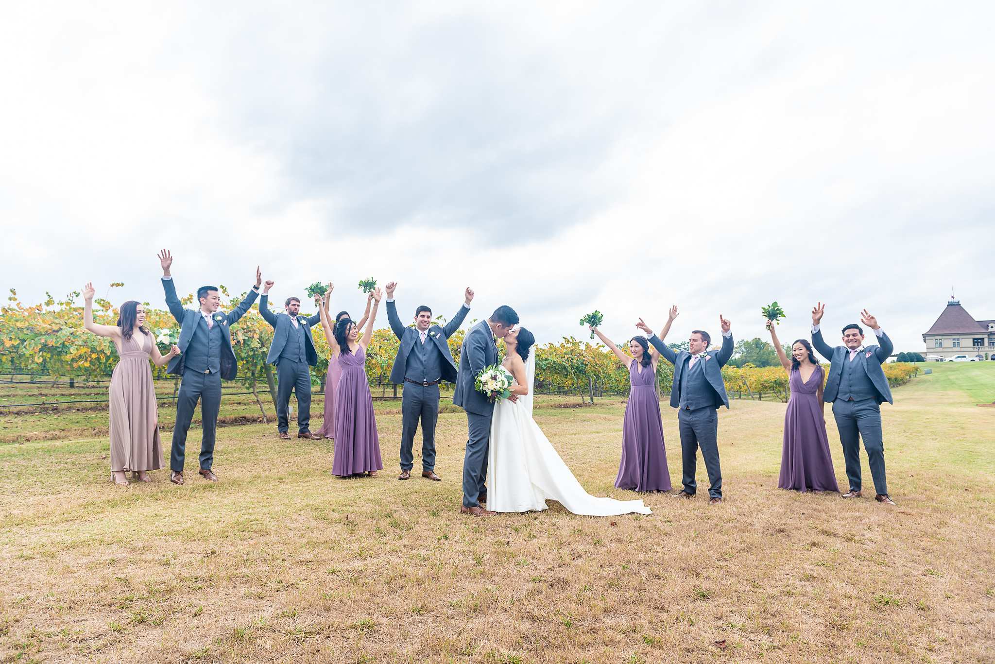 Wedding party cheers with arms raised in the vineyard field with the Chateau Elan chateau behind them