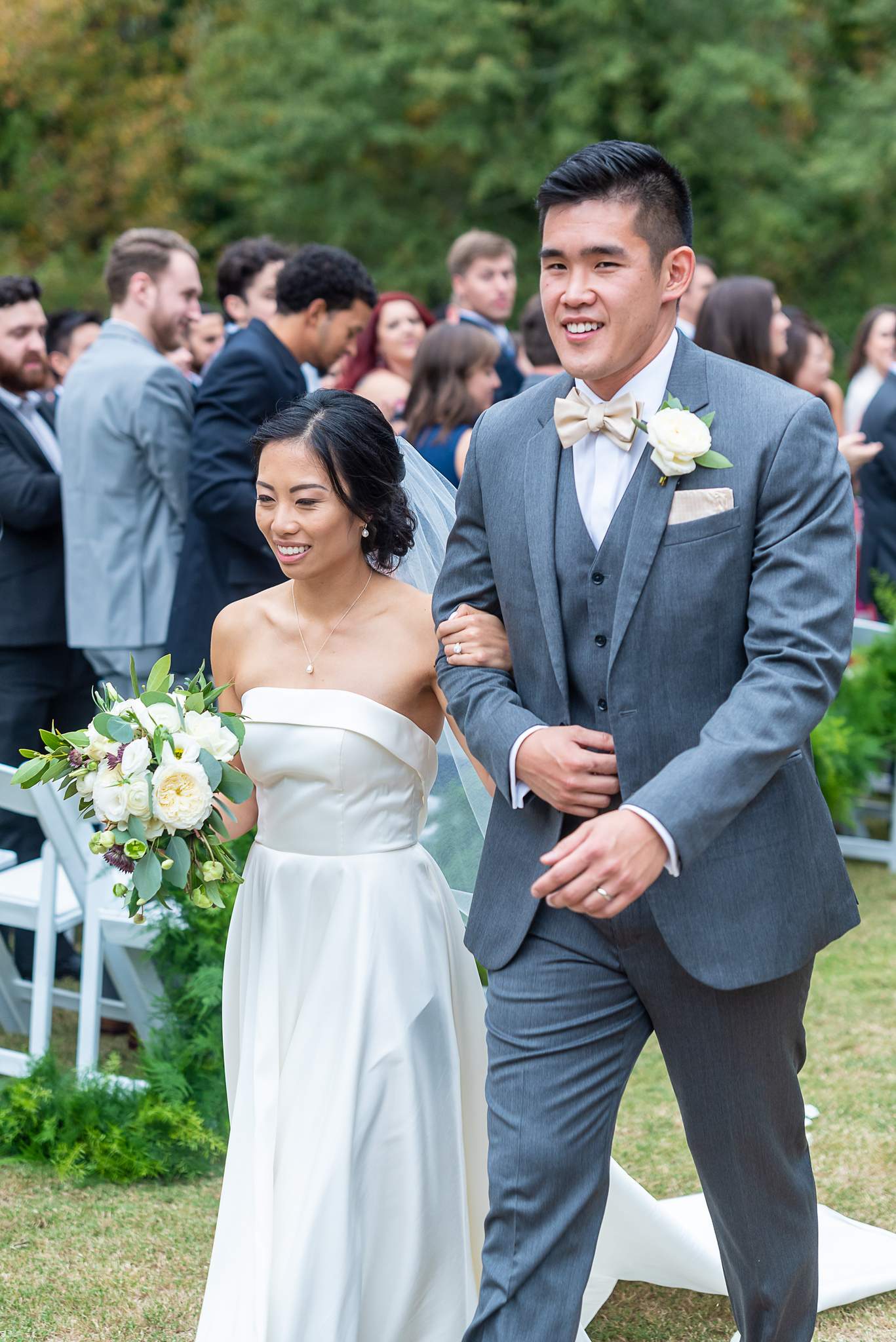 Smiling bride and groom walk back up the aisle past cheering guests after the ceremony