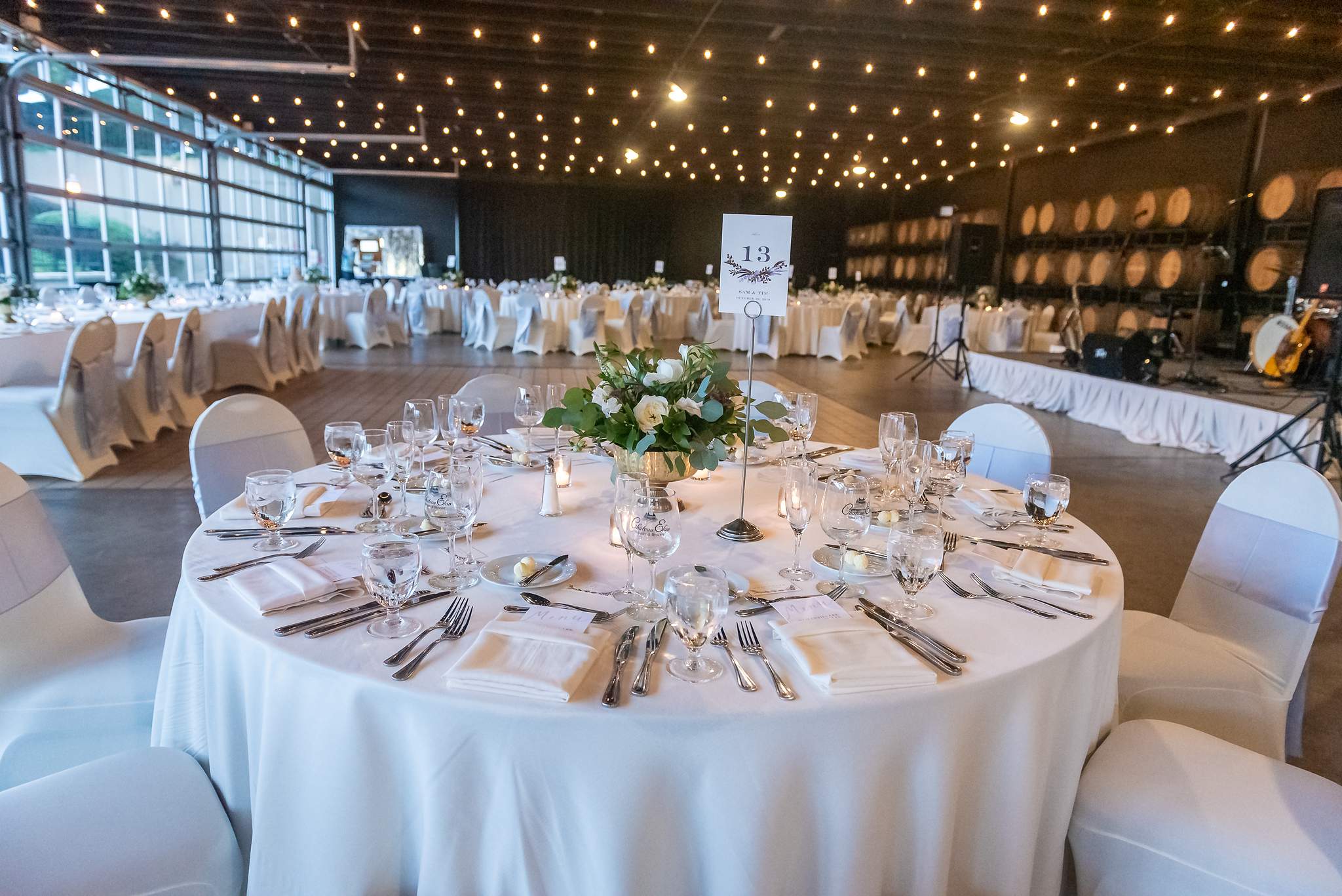 Round table with white linens and greenery set for the reception under string lights