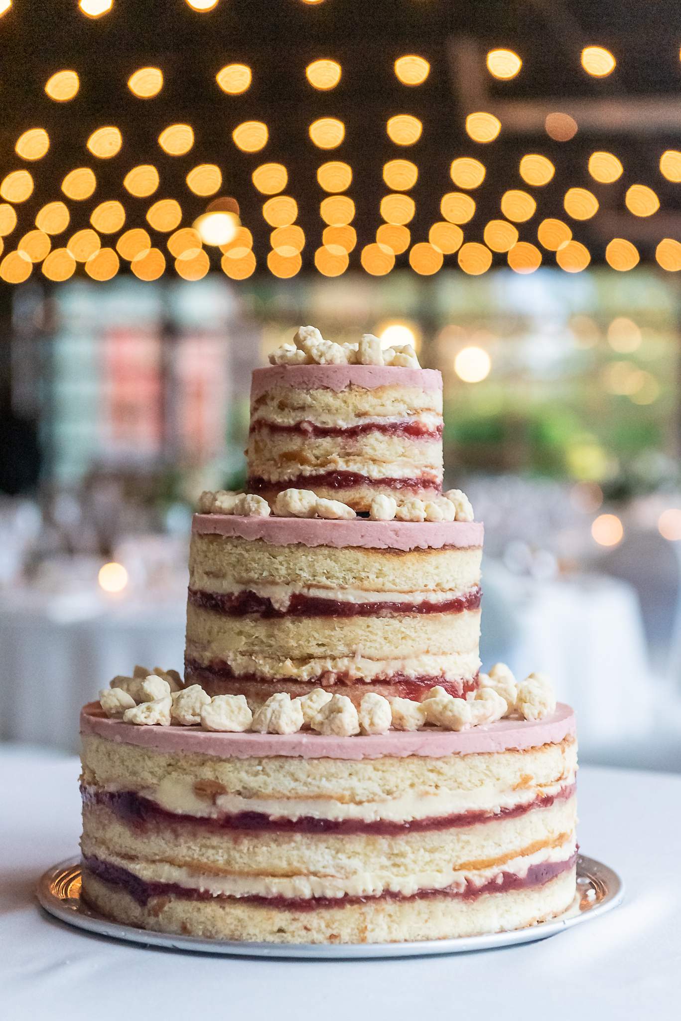 Three-tier naked cake with berry filling and meringue topping under glowing string lights