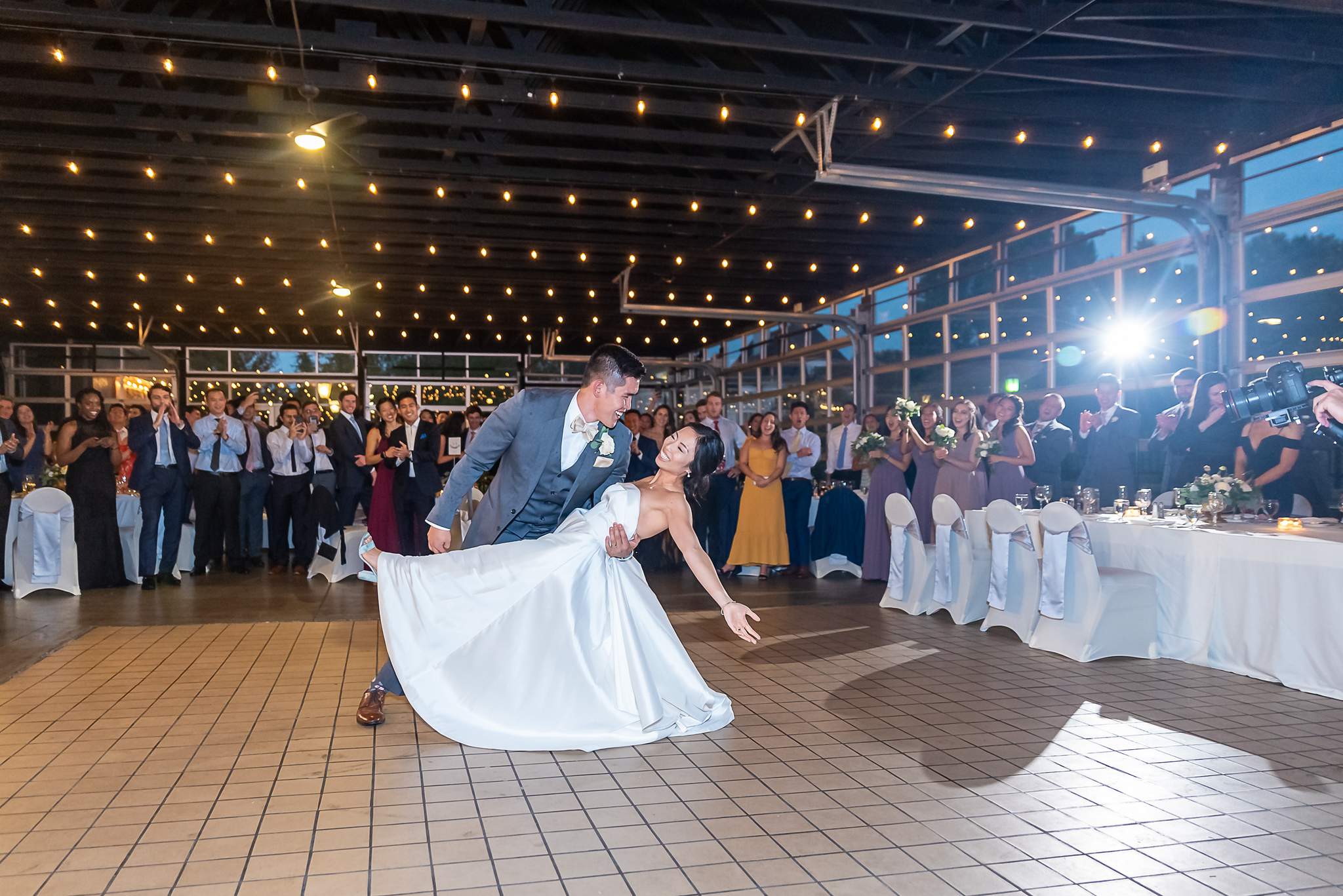 Groom dips the bride during their first dance in the string-lit reception hall at Chateau Elan