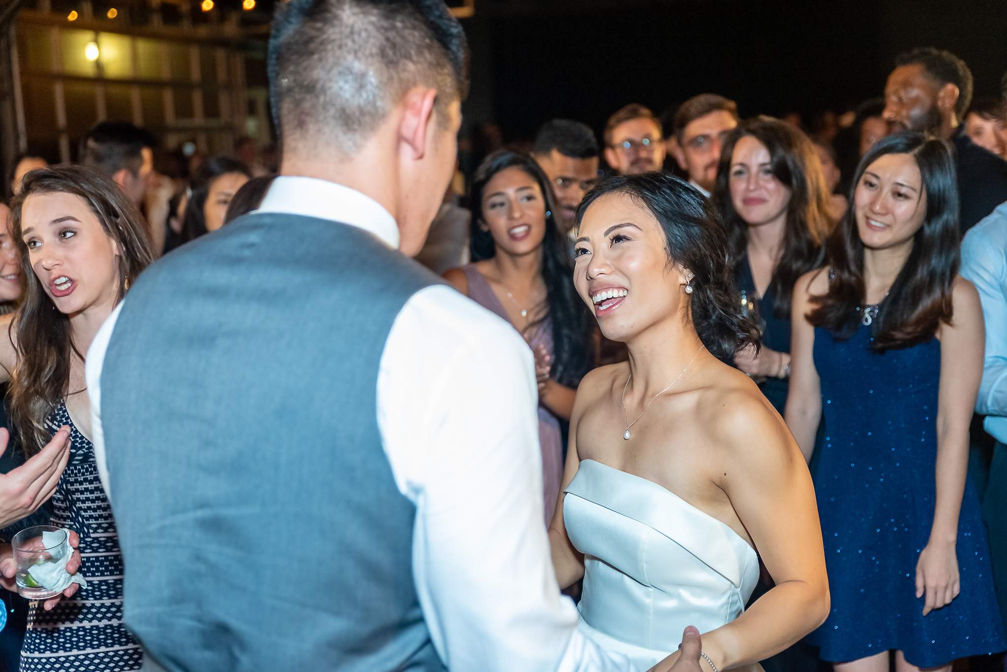 Bride laughs while dancing with the groom among friends on the reception dance floor