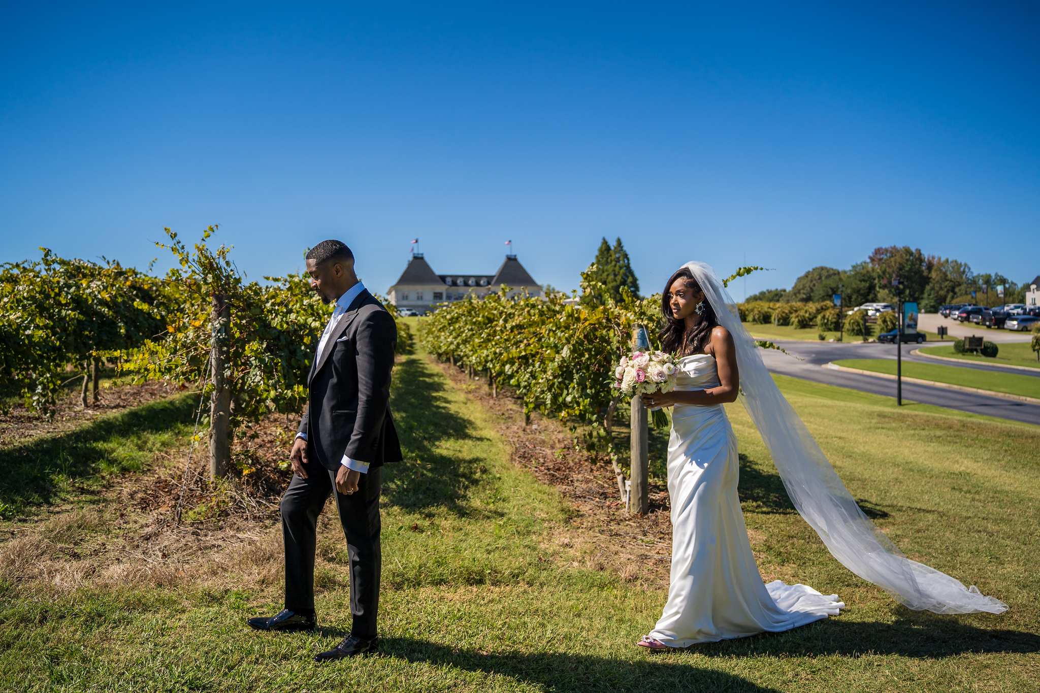 Groom waits in the vineyard rows as the bride approaches for their first look at Chateau Elan