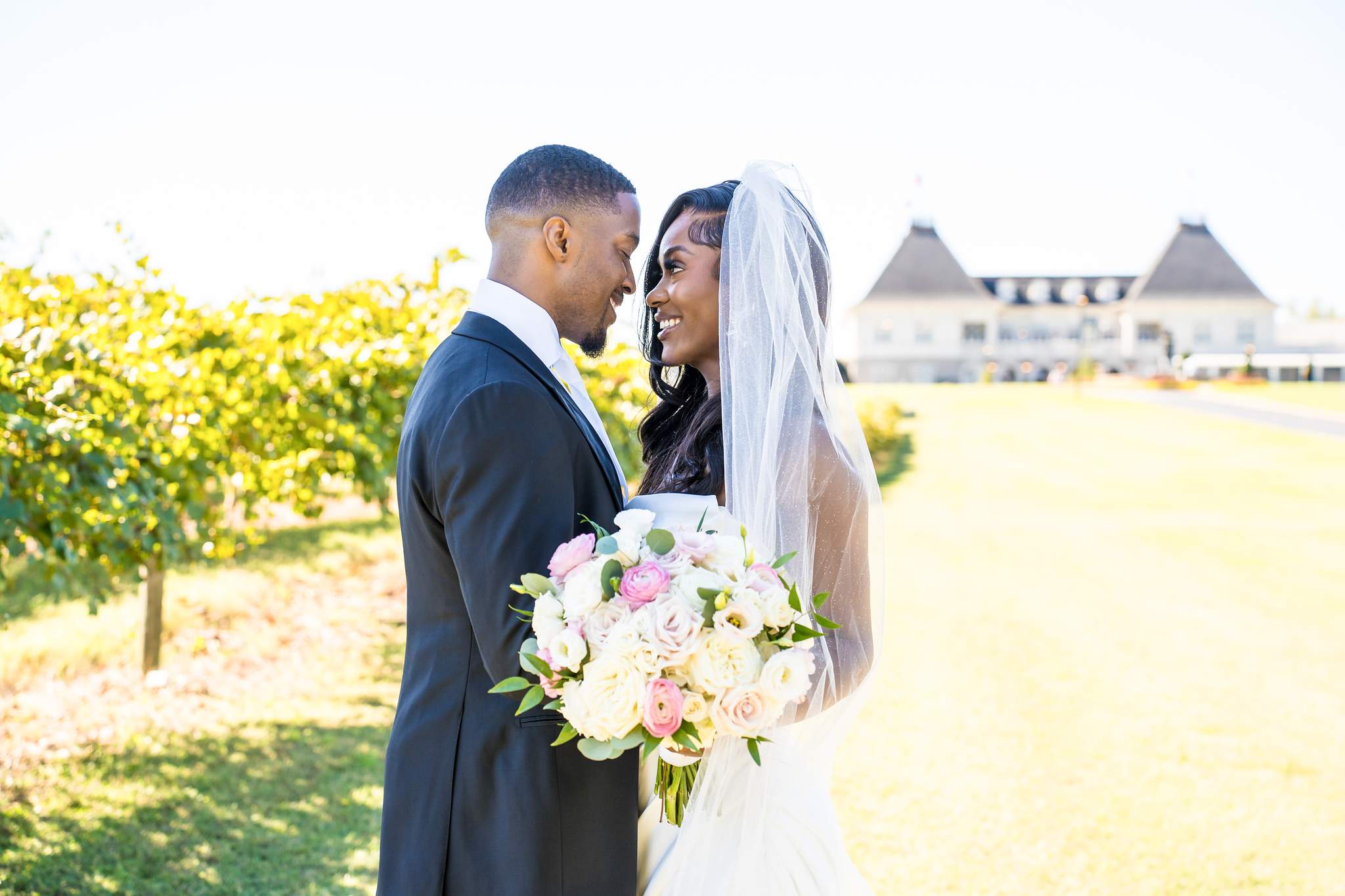 Bride and groom share a smile in the vineyard with the Chateau Elan chateau behind them