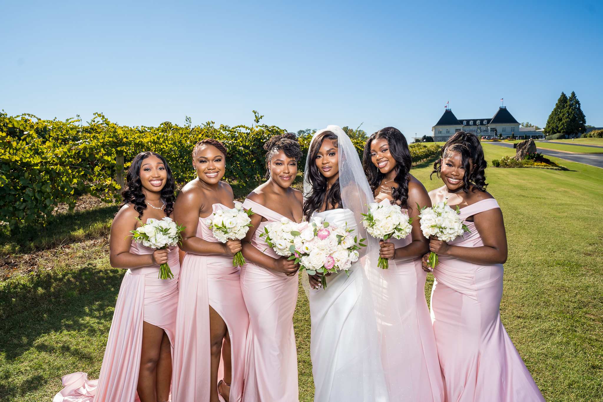 Bride and bridesmaids in blush pink gowns hold bouquets in the Chateau Elan vineyard