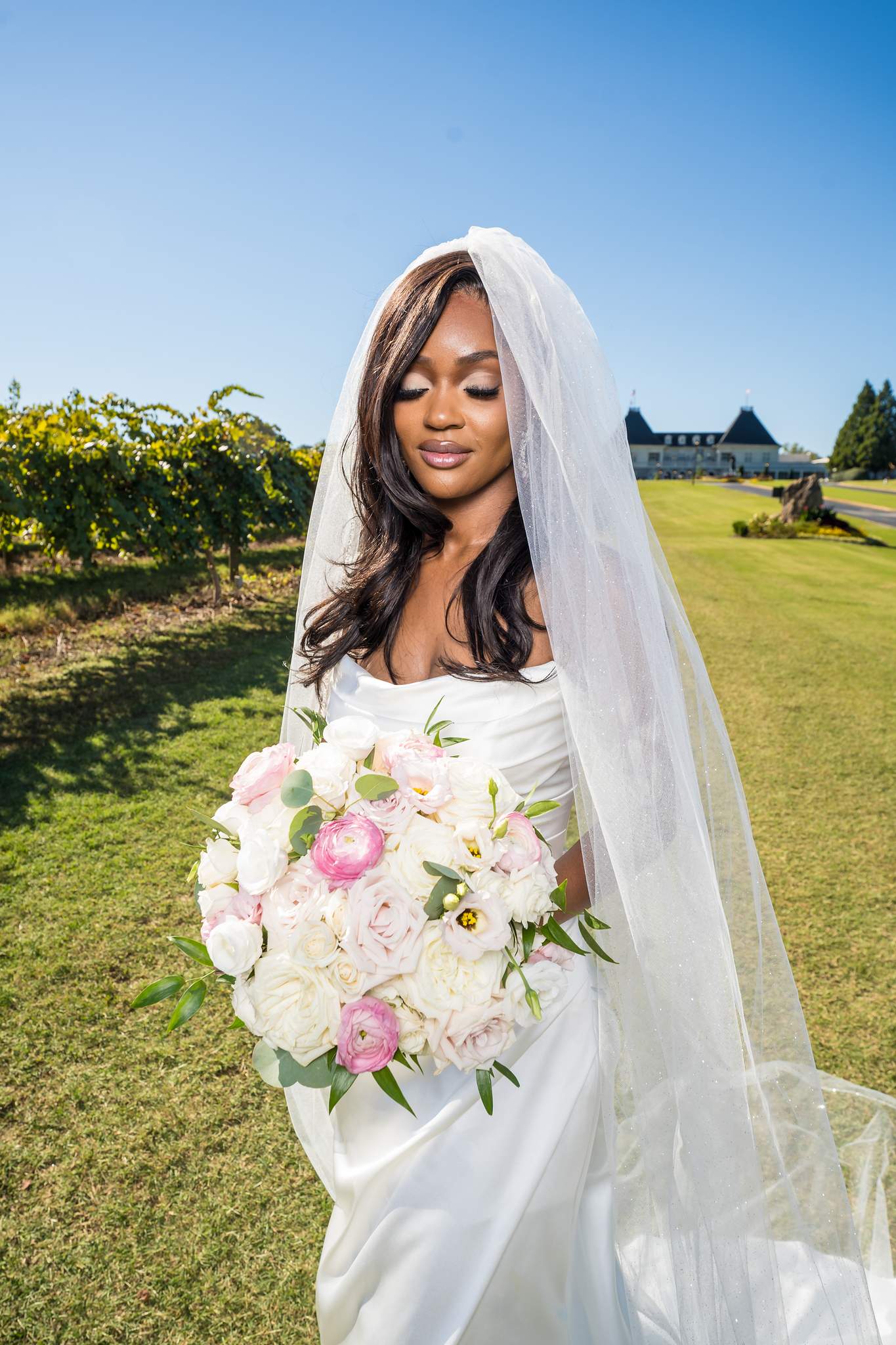 Bride holds a pink and white bouquet in the vineyard with Chateau Elan in the distance