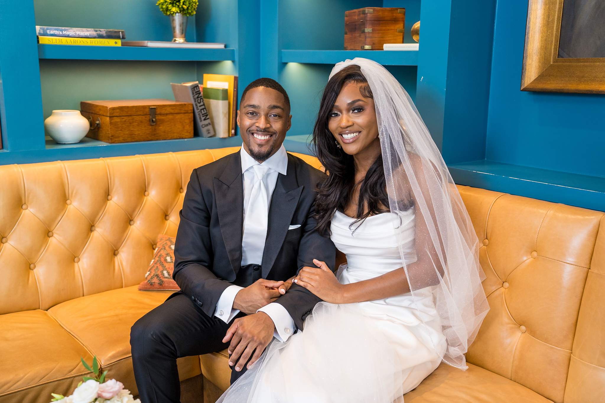 Bride and groom sit on a caramel leather sofa in a teal lounge at Chateau Elan