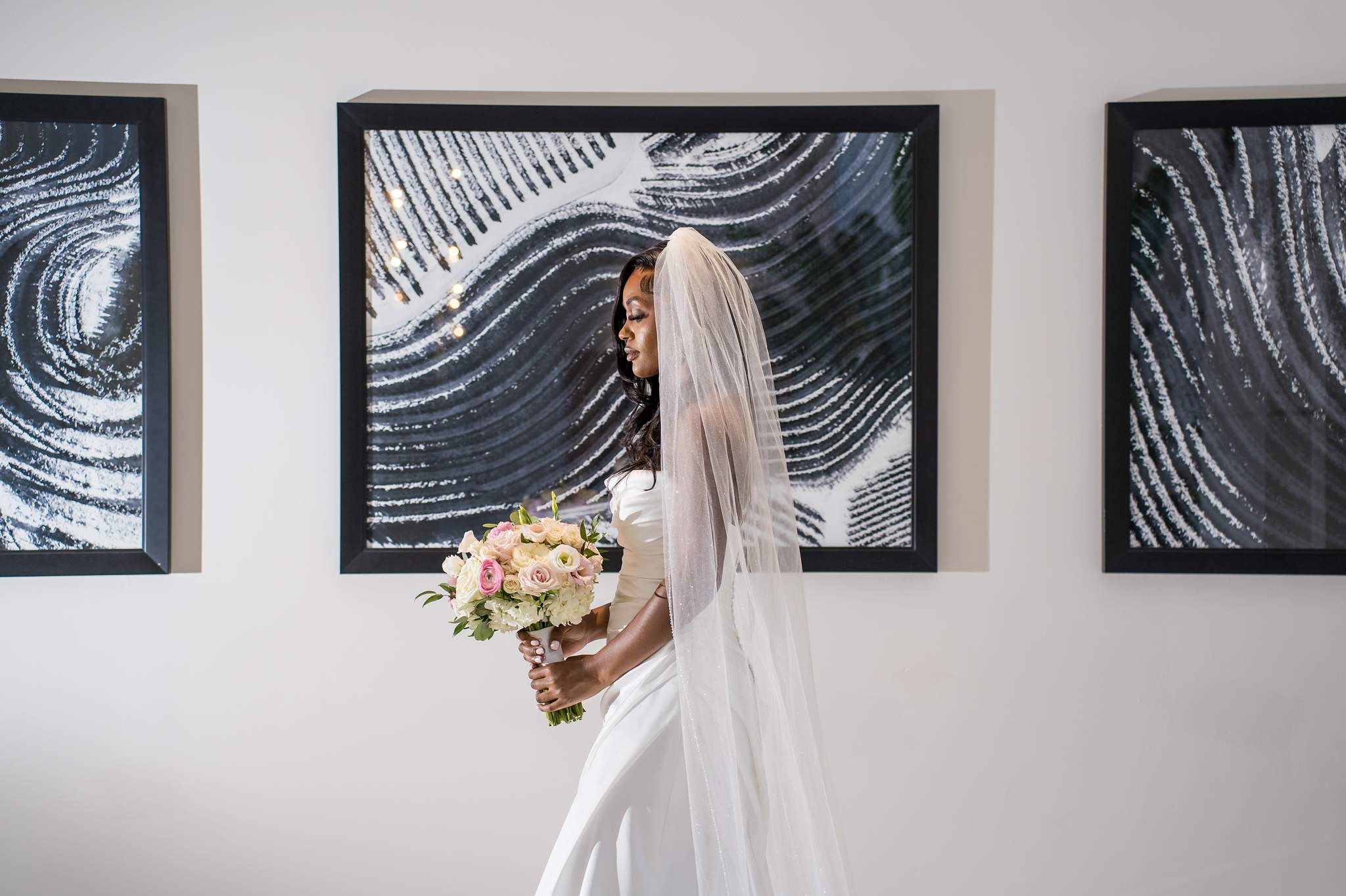 Bride with veil and bouquet stands between large black and white artworks in a Chateau Elan hallway