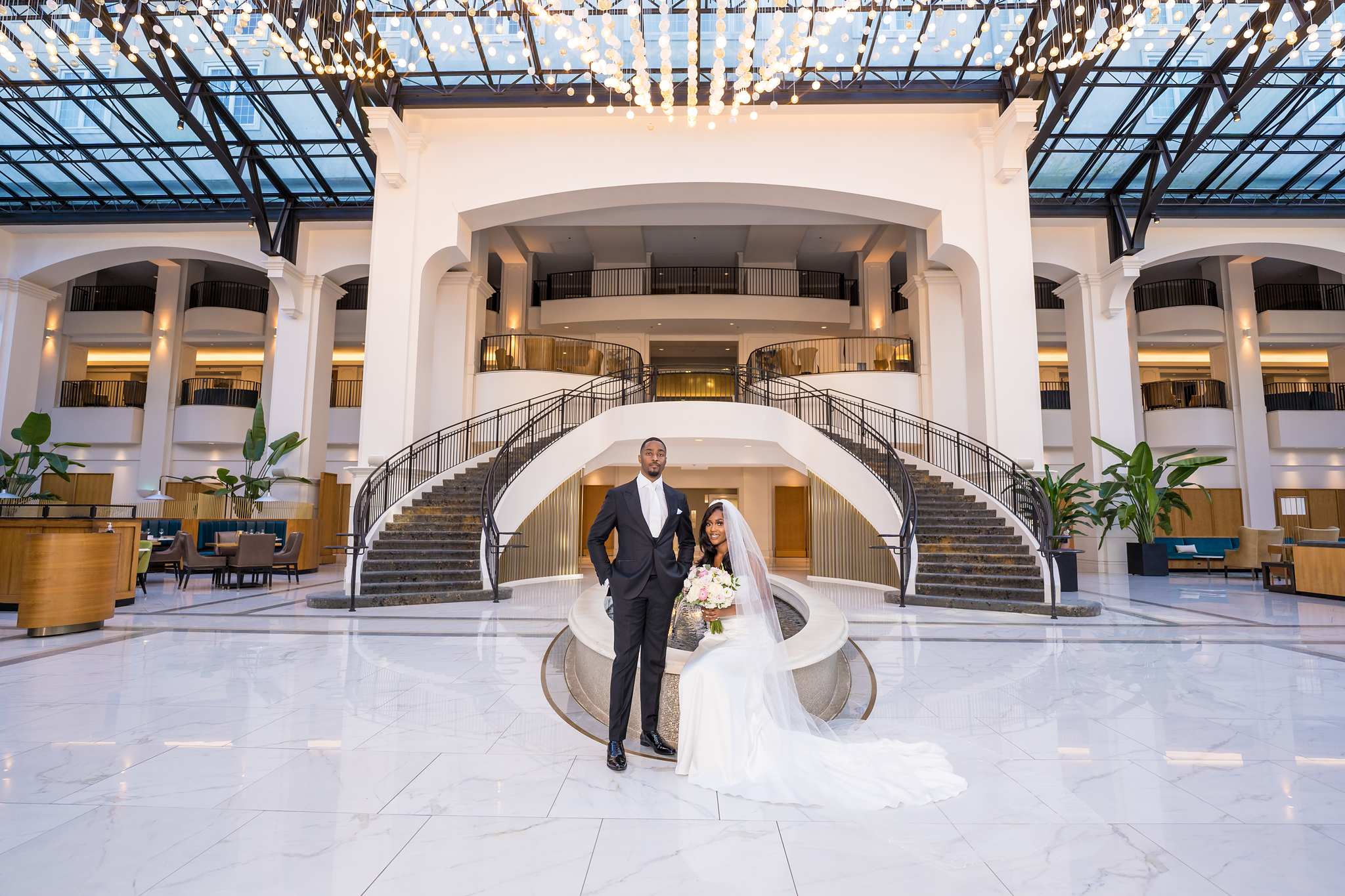 Bride and groom stand in the grand Chateau Elan atrium beneath the glass roof and curved staircases