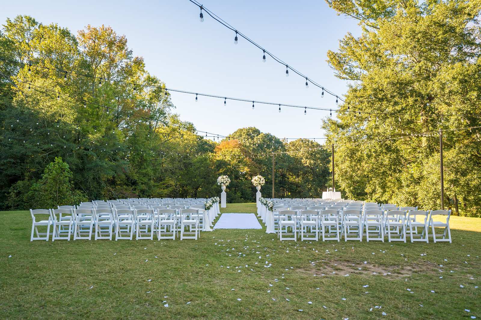 Empty ceremony lawn with white chairs, floral aisle stands and string lights at Chateau Elan