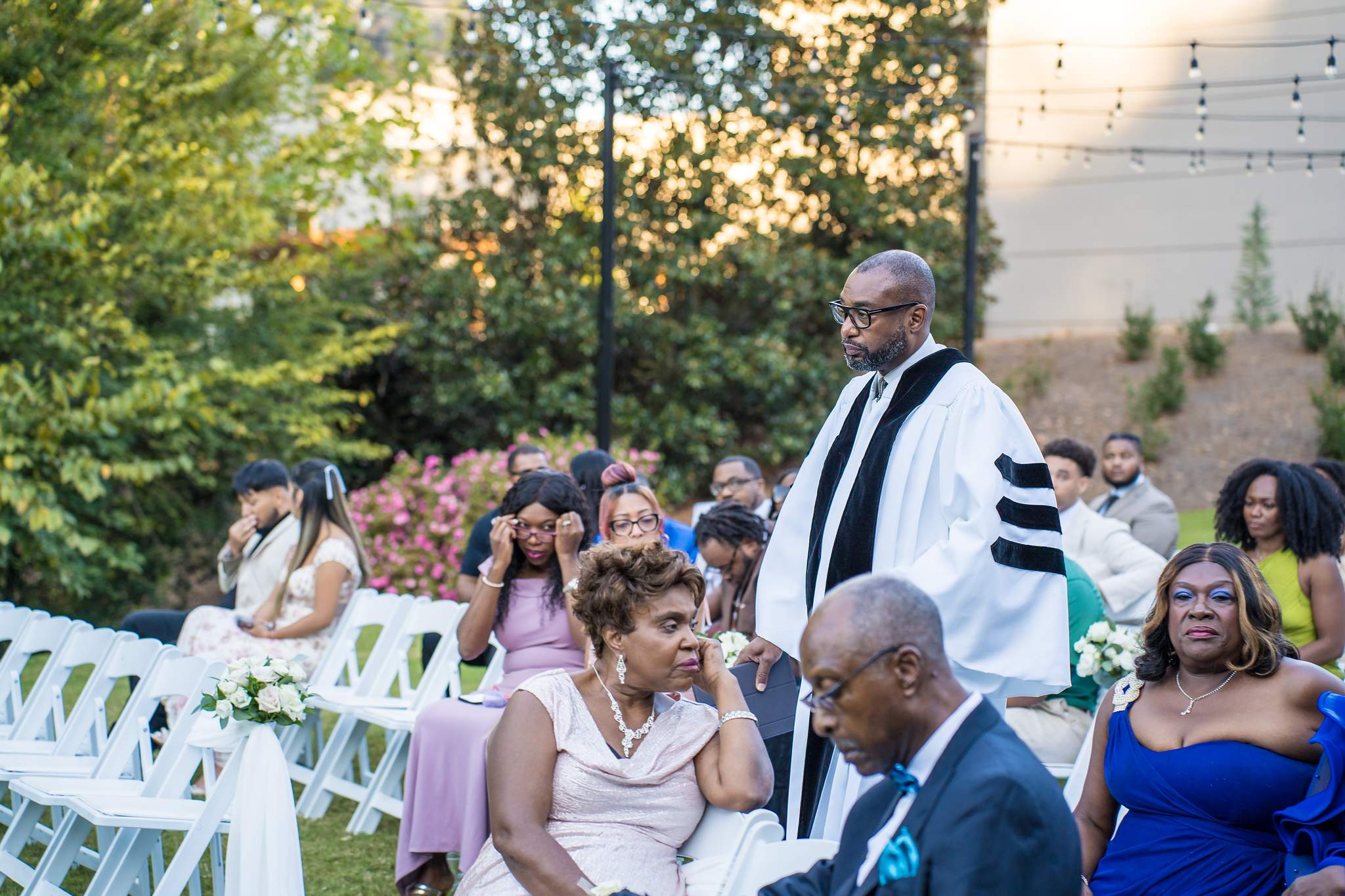 Officiant in a black and white robe walks up the aisle past seated guests