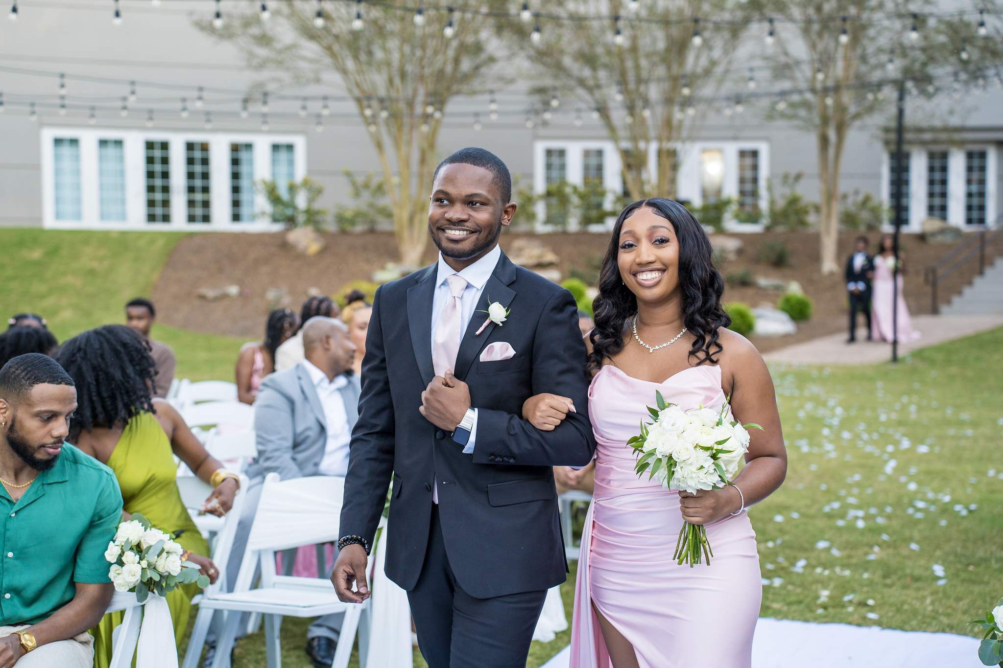 Smiling groomsman and bridesmaid walk arm in arm during the processional on the Chateau Elan lawn