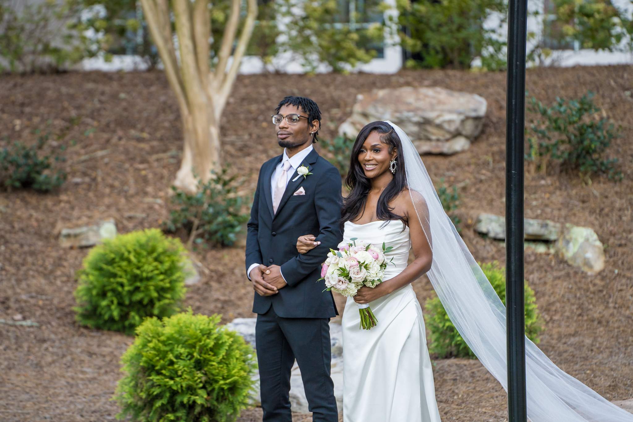 Bride waits with a family member beside the landscaped garden before walking down the aisle