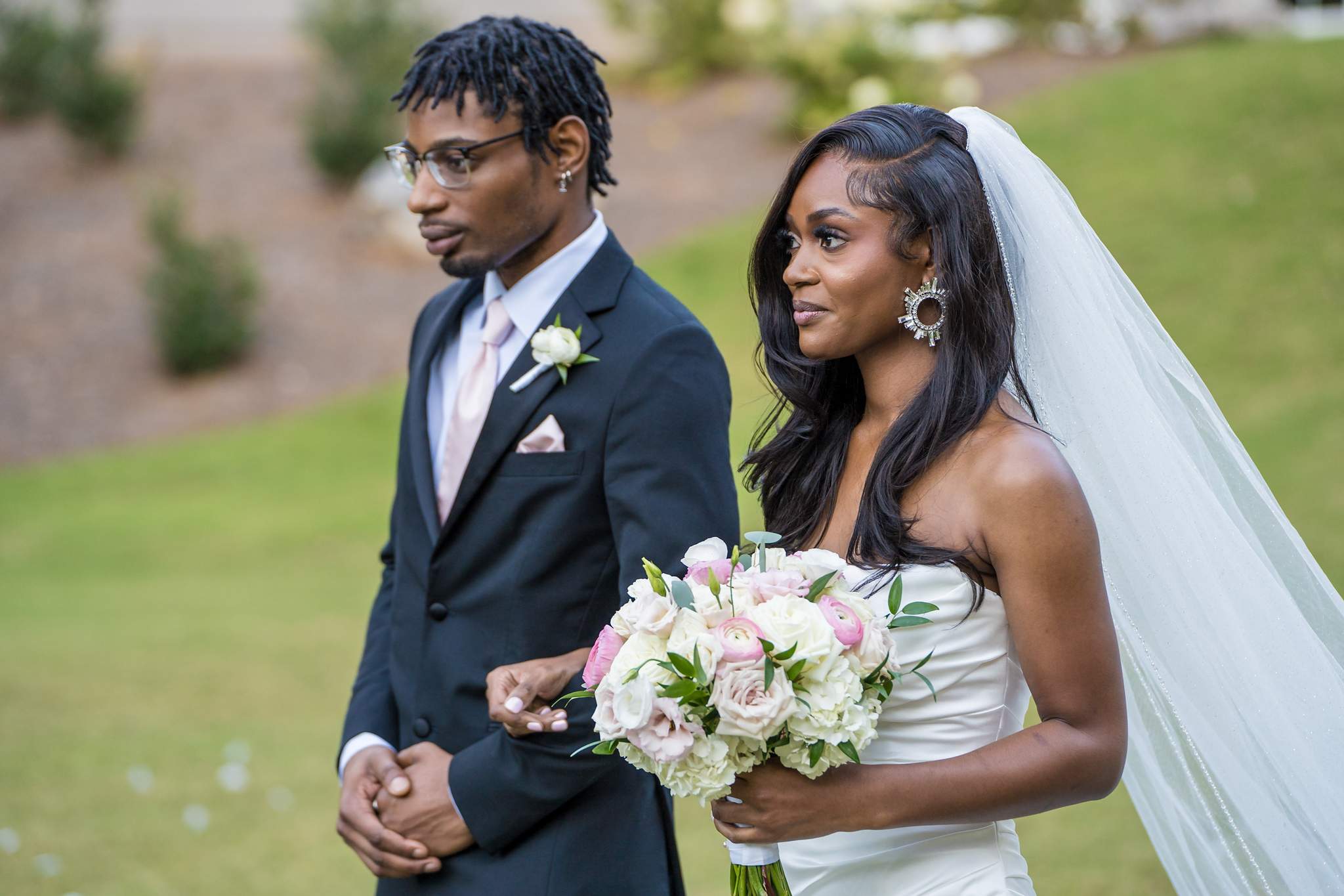 Bride and a family member walk arm in arm toward the ceremony, her bouquet in pink and white