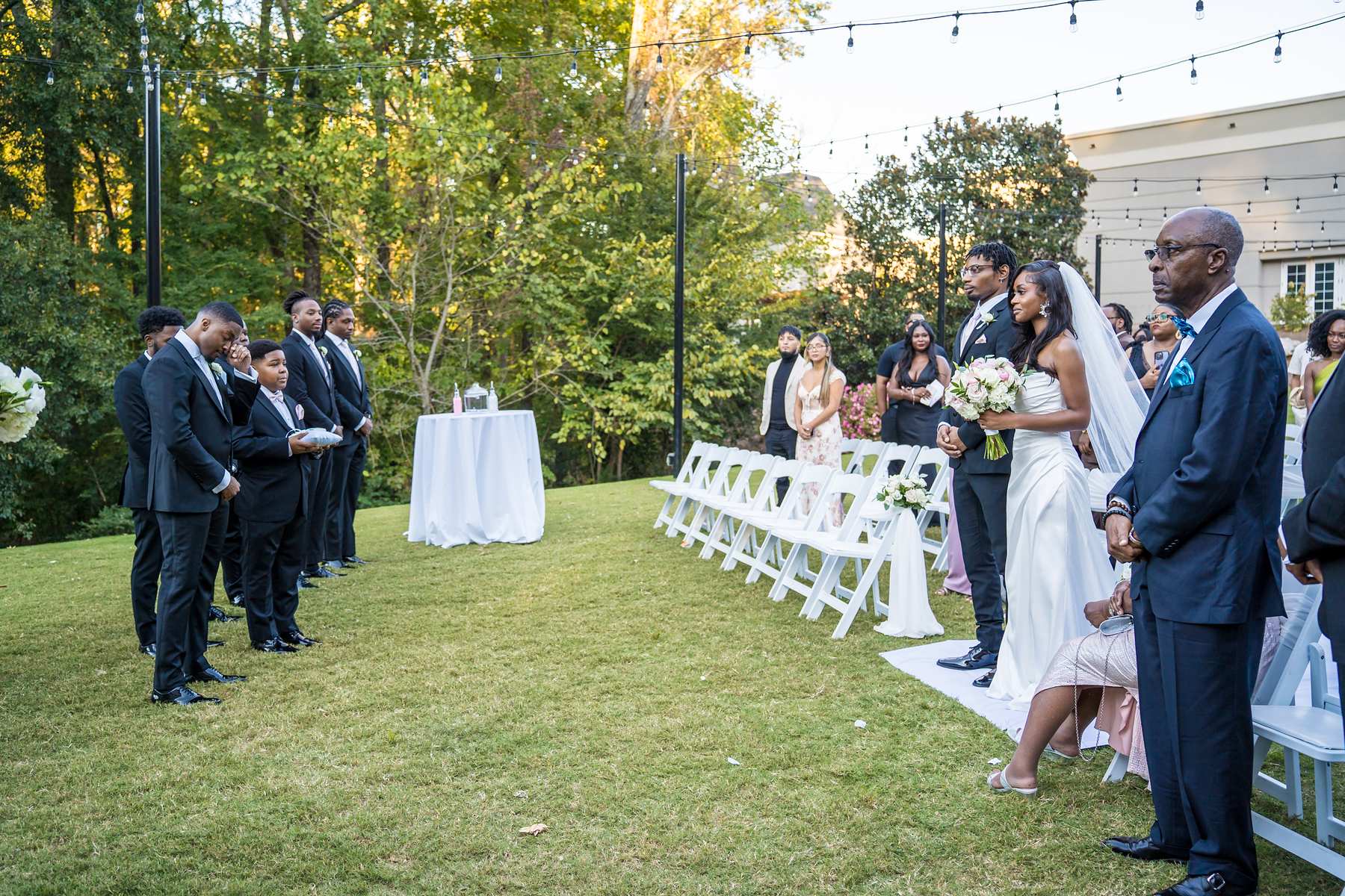 Groomsmen look on as the bride arrives at the end of the aisle on the ceremony lawn